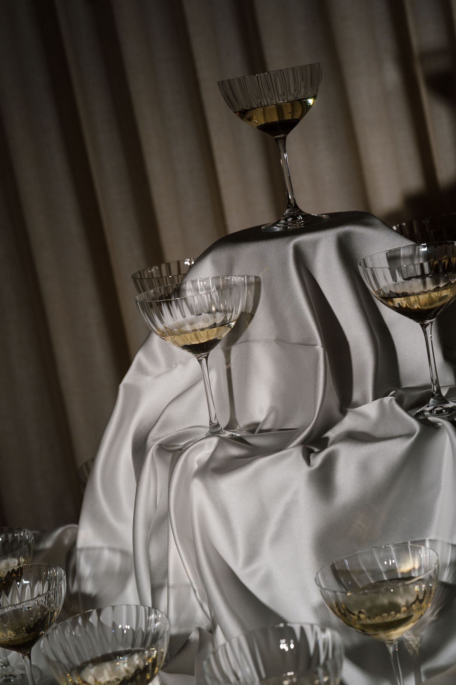 Elegant champagne tower with crystal coupe glasses arranged on white satin fabric at a wedding reception.