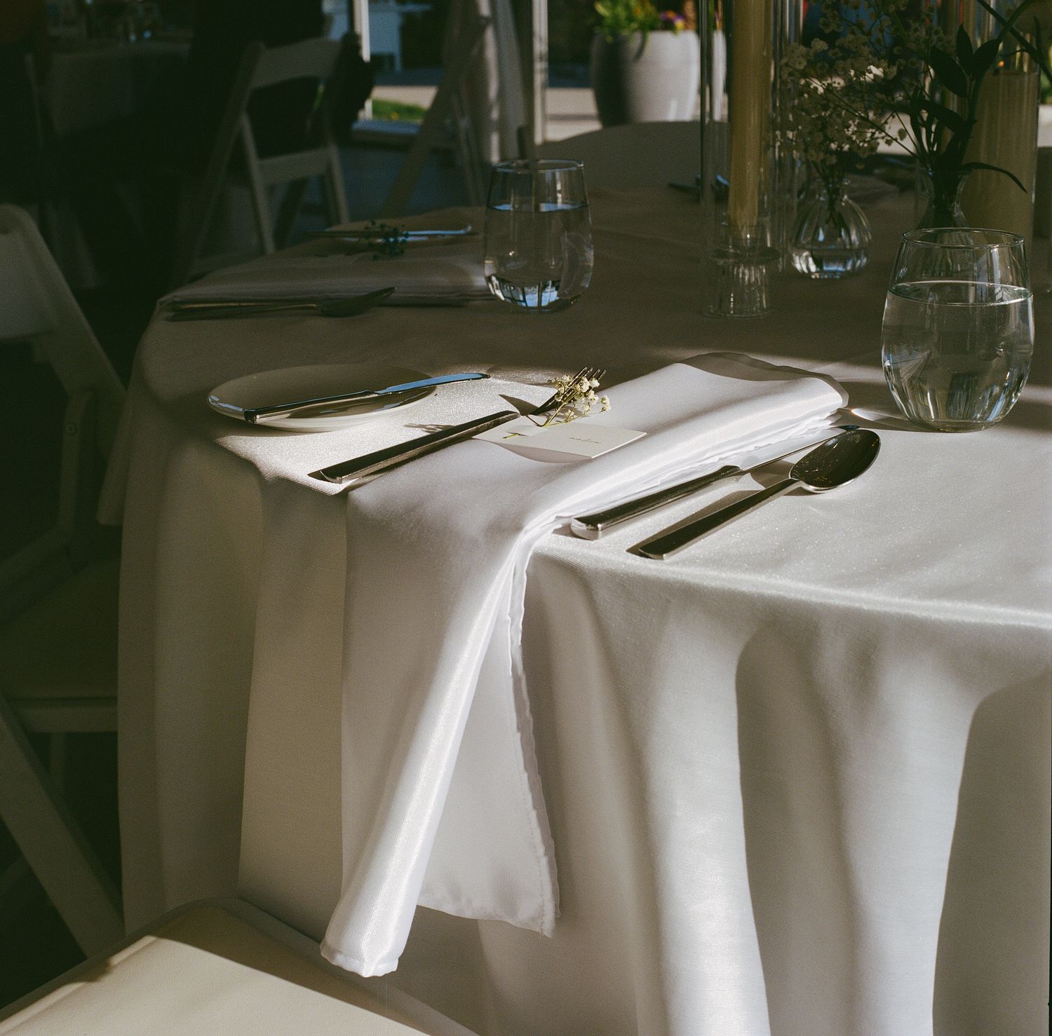 An elegant restaurant table setting with white linens, silverware, and wine glasses arranged on a crisp tablecloth.