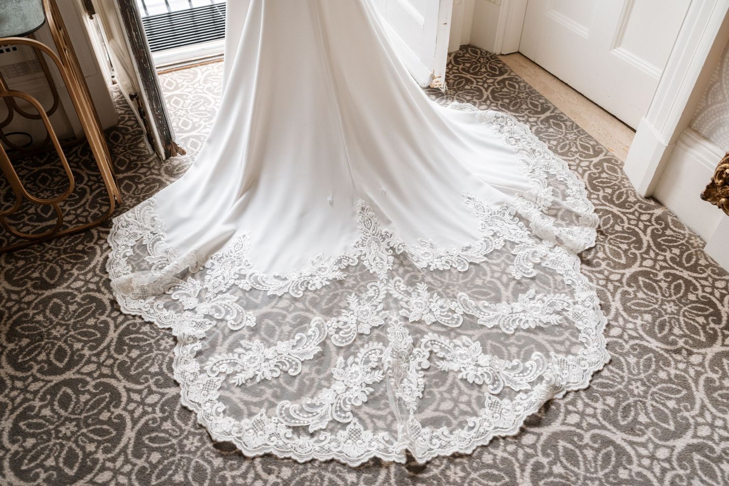 A flowing white lace wedding dress train elegantly draped across an ornate patterned floor.
