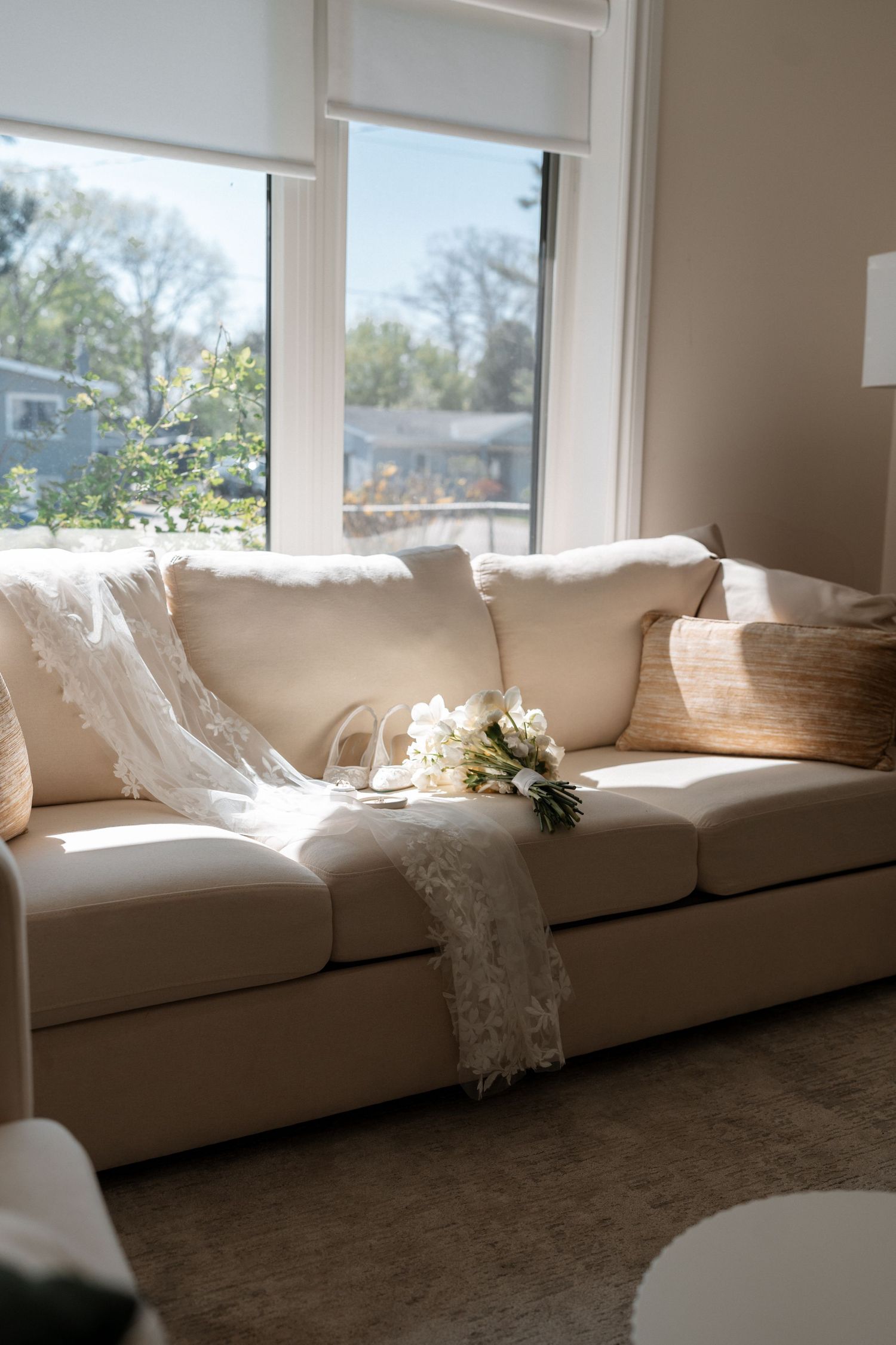 Sunlit cream couch with delicate lace throw and white flowers by a bright window in a cozy living room.