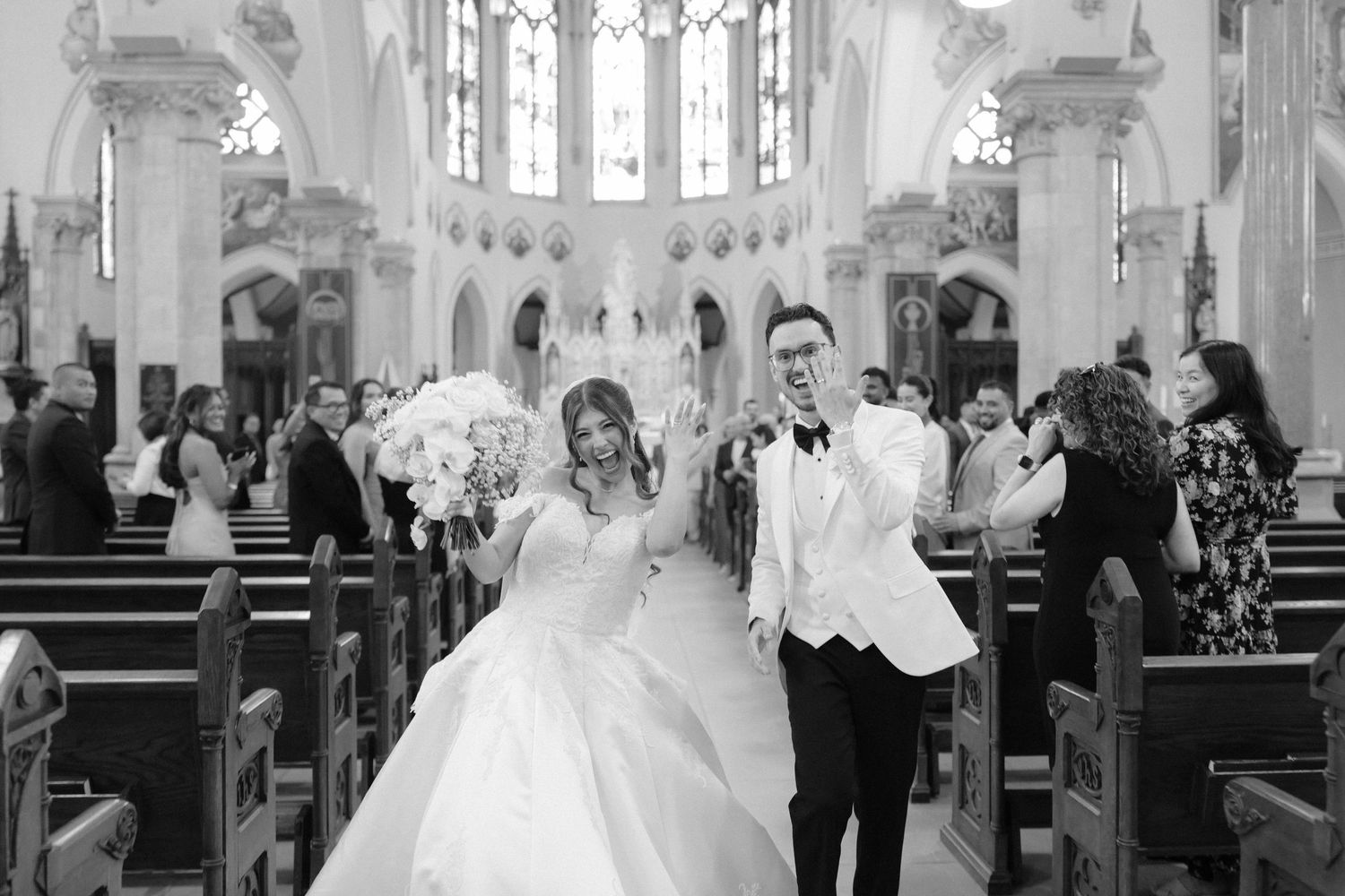 Bride and groom walk down church aisle after wedding ceremony in black and white photo.