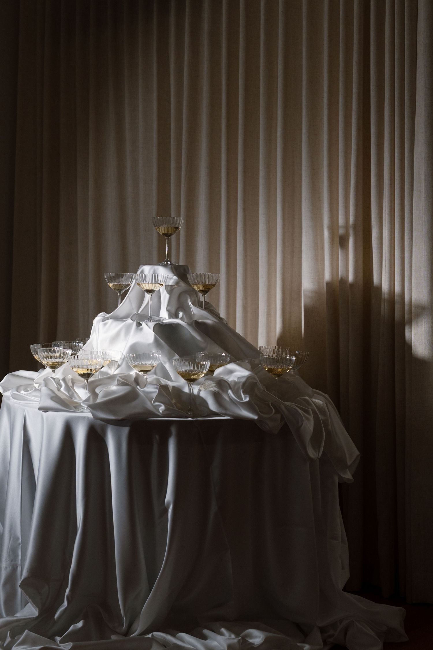 Champagne tower with crystal coupe glasses draped in white satin on a round table.