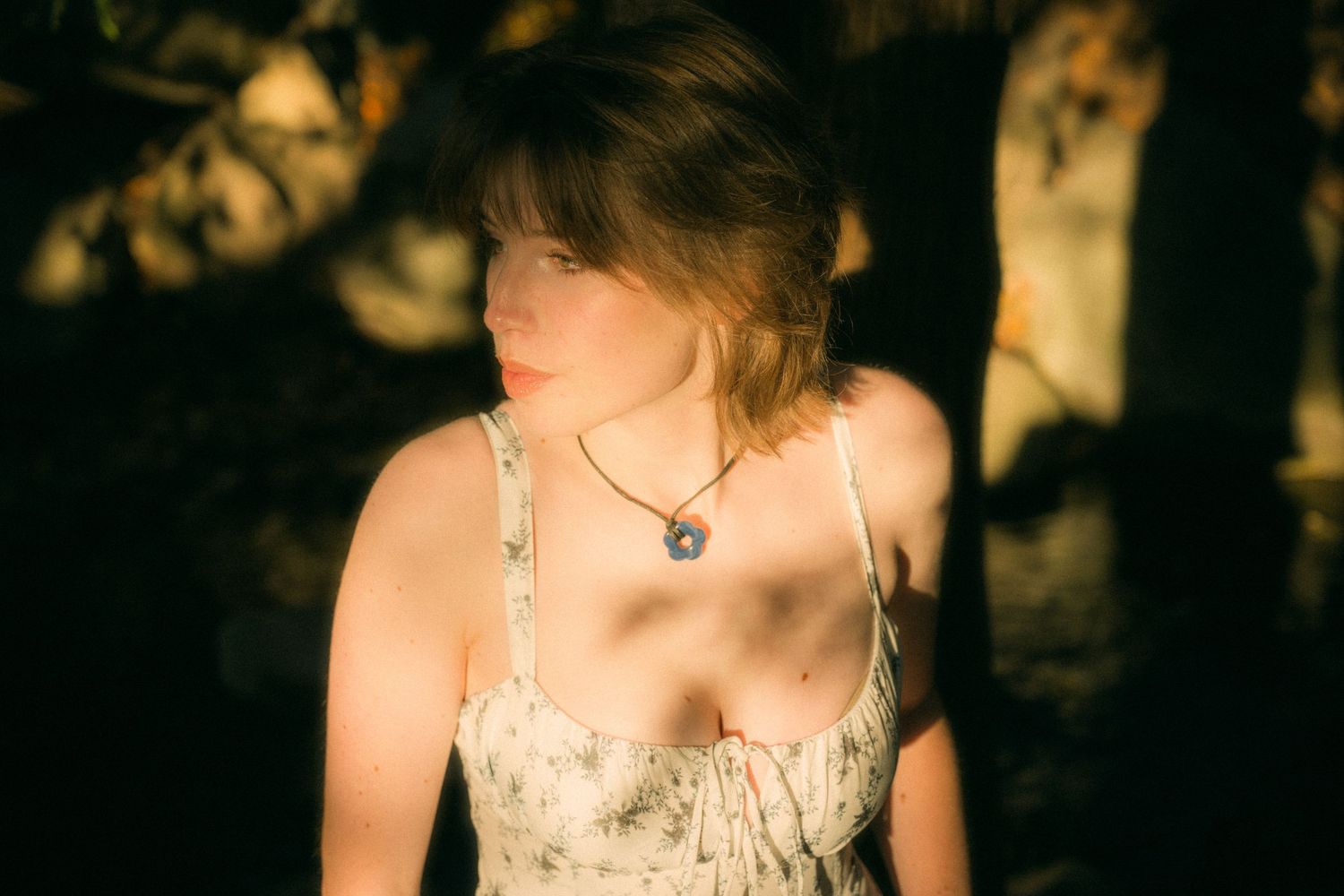 A person wearing a light colored dress stands in dappled sunlight.