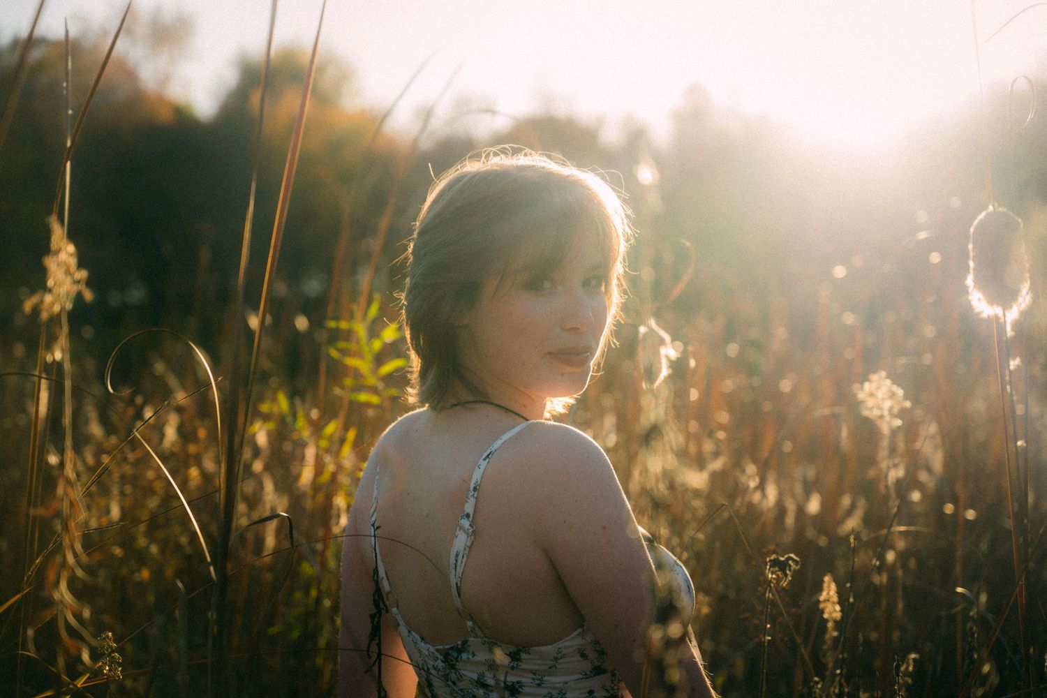 Figure backlit by golden sunlight standing in a field of tall grass at sunset.