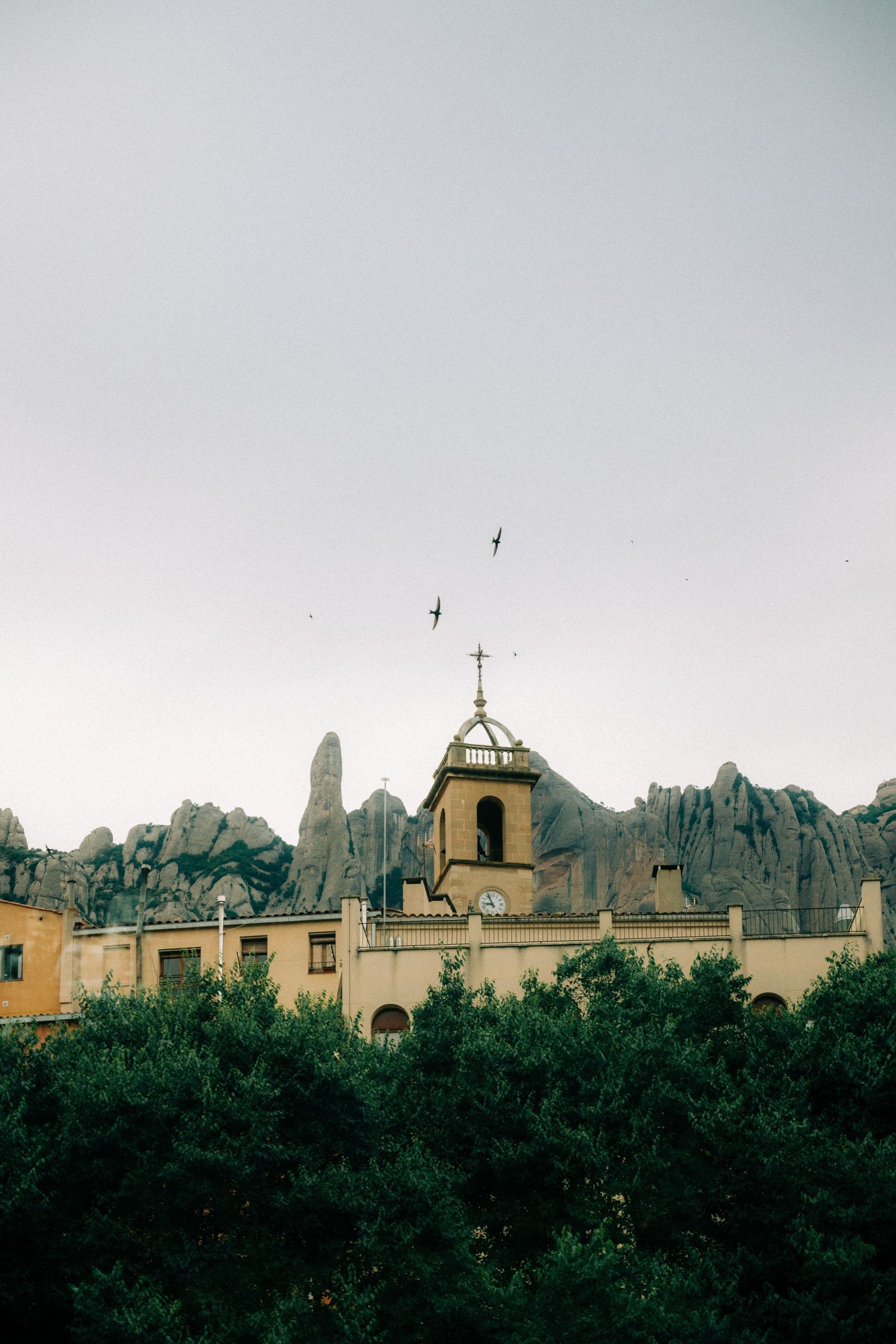 Historic monastery building with bell tower set against dramatic rocky mountain peaks.