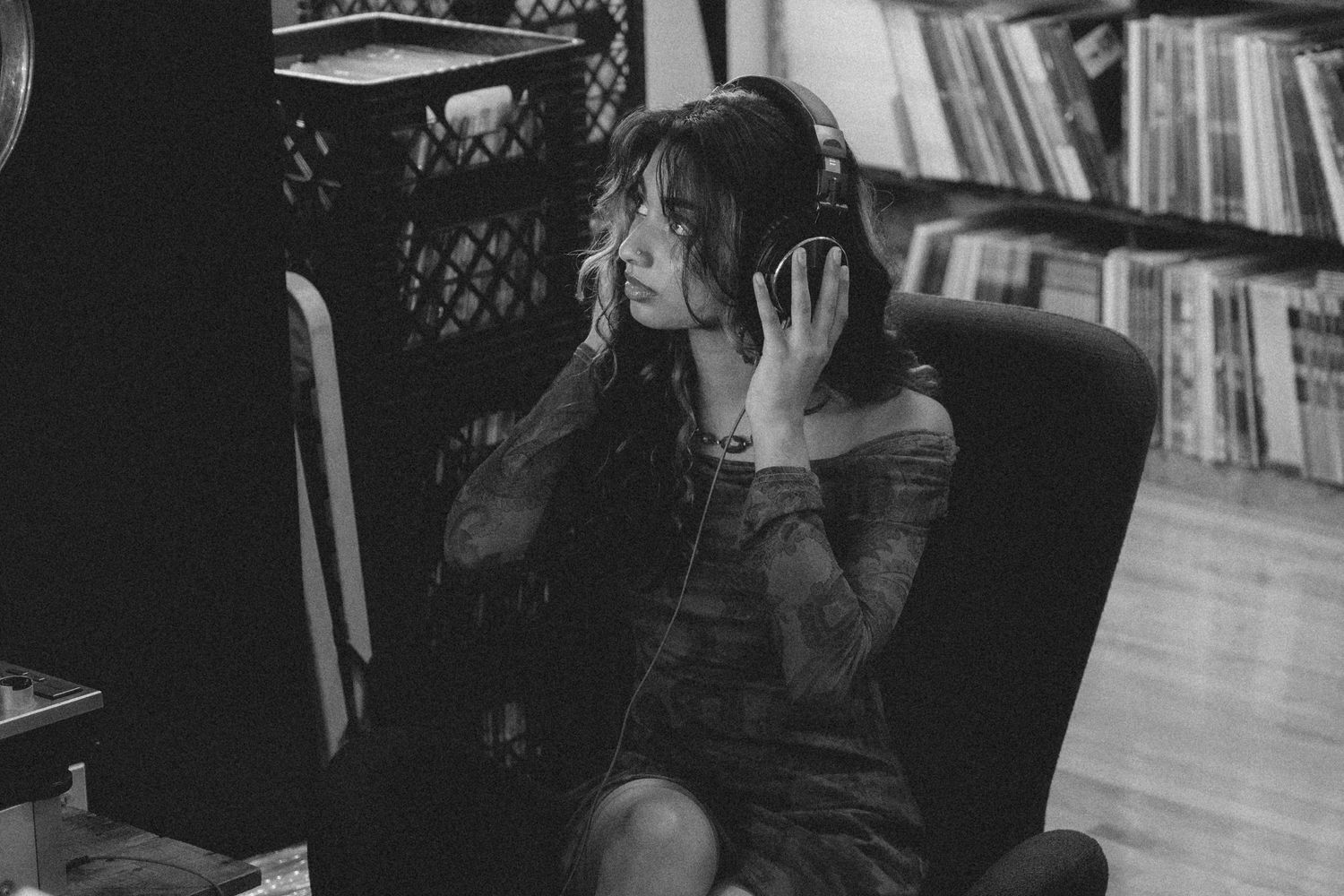 Person wearing headphones sitting in a chair surrounded by bookshelves in a moody black and white setting.