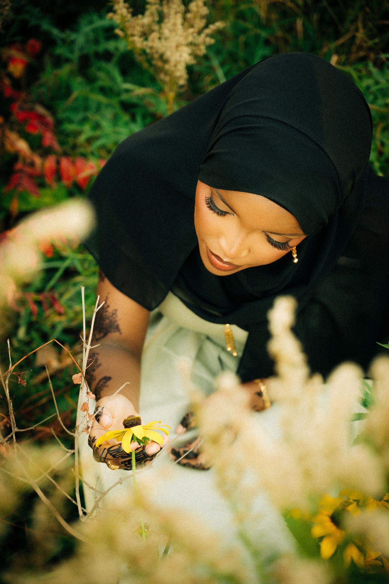 Close-up of someone in black hijab examining flowers in a garden setting.