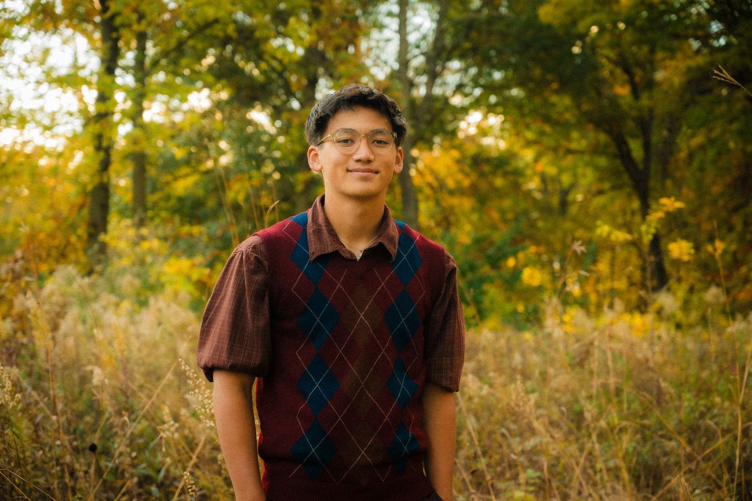 Portrait in a brown argyle sweater standing in autumn foliage with golden sunlight.