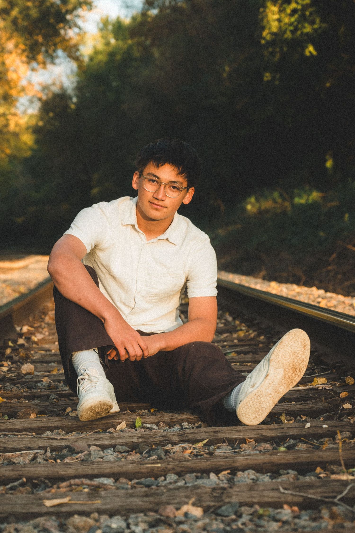 Person sitting casually on railroad tracks during golden hour photography session.