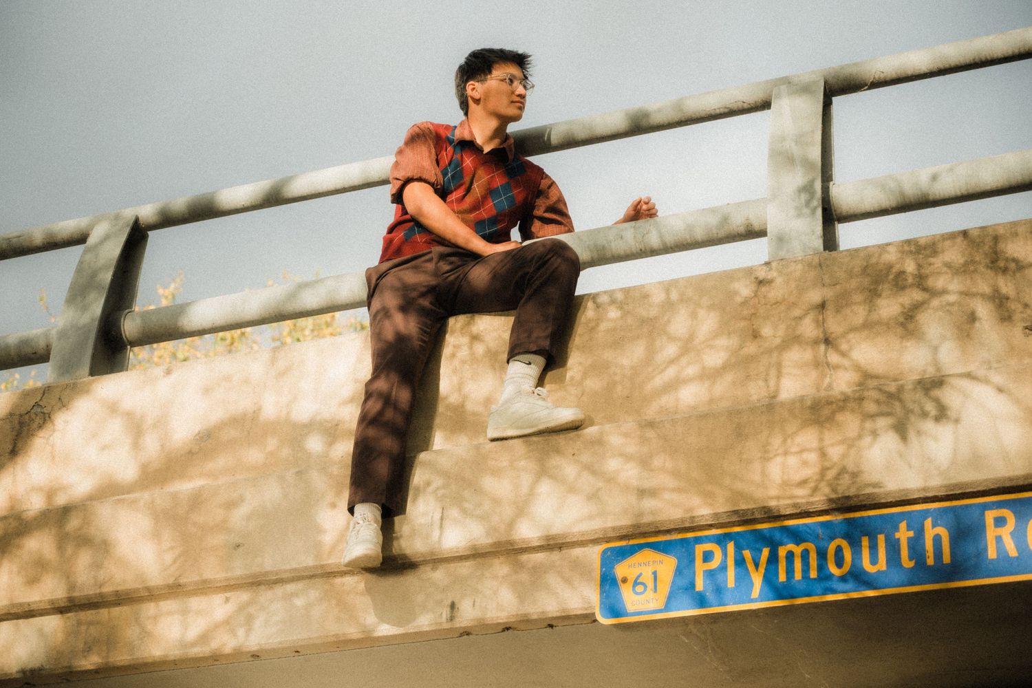 Person sitting on Plymouth Road sign structure during golden hour photography session.