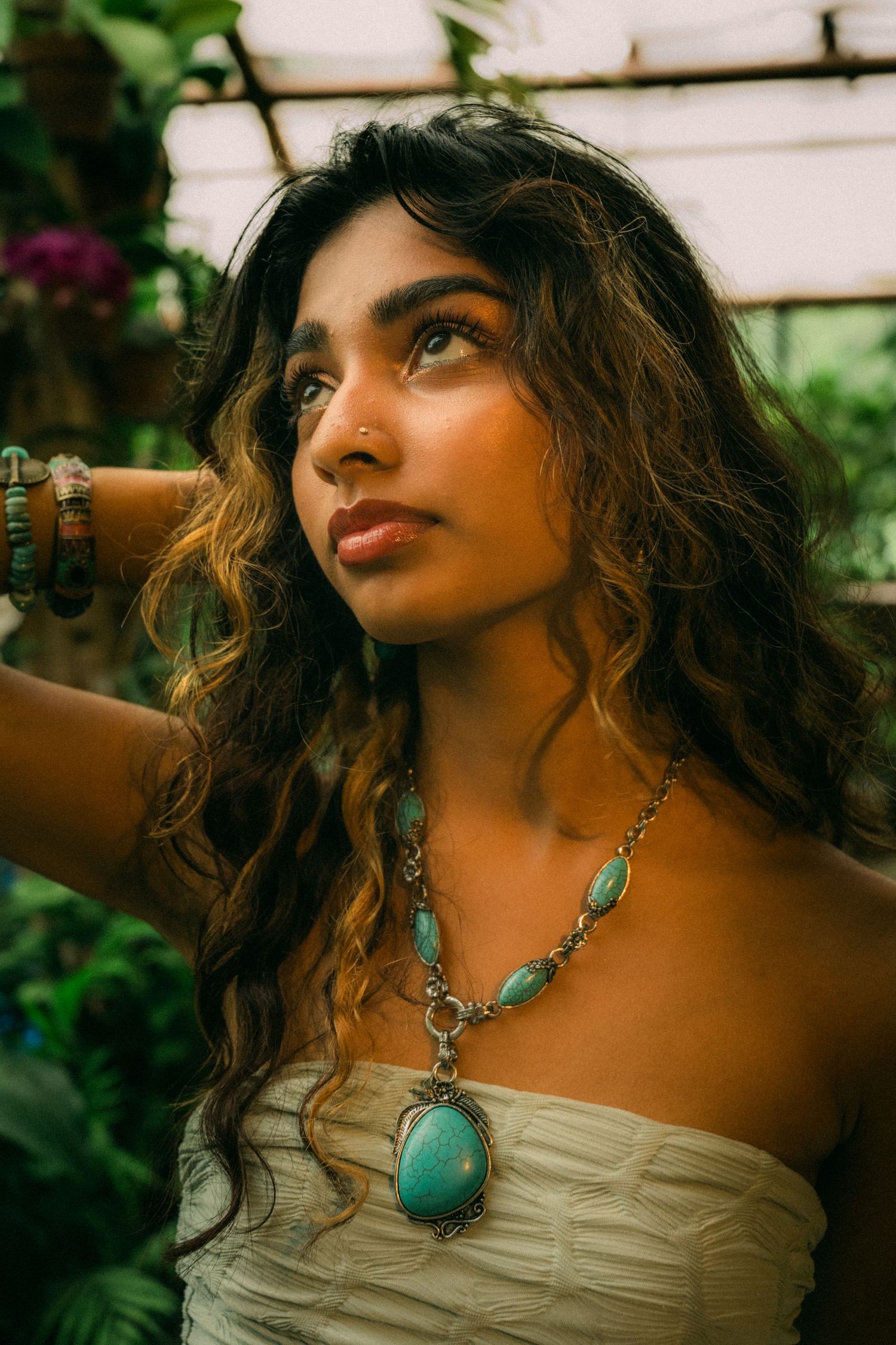 A close-up portrait featuring a turquoise statement necklace against a garden background.