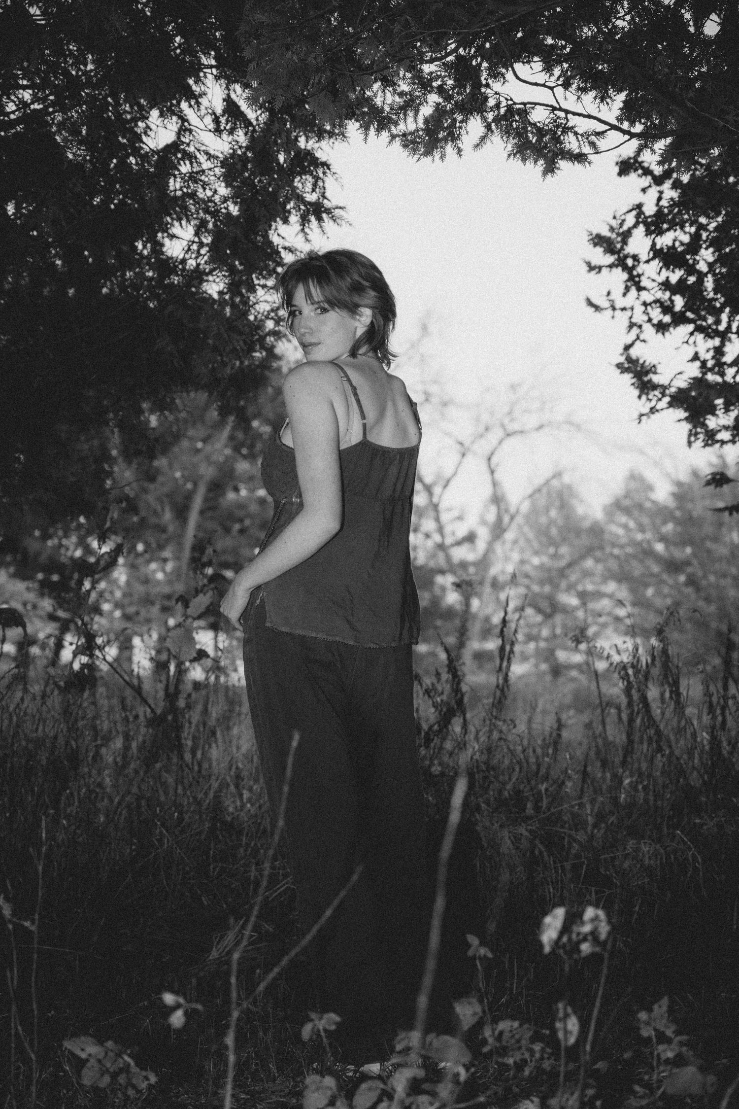 Artistic black and white portrait in natural setting with trees framing the subject.