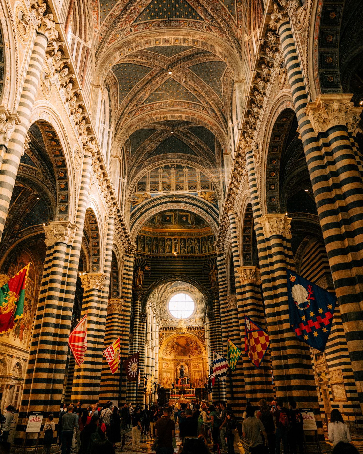 Ornate cathedral interior with striped marble columns and vaulted ceilings adorned with flags.