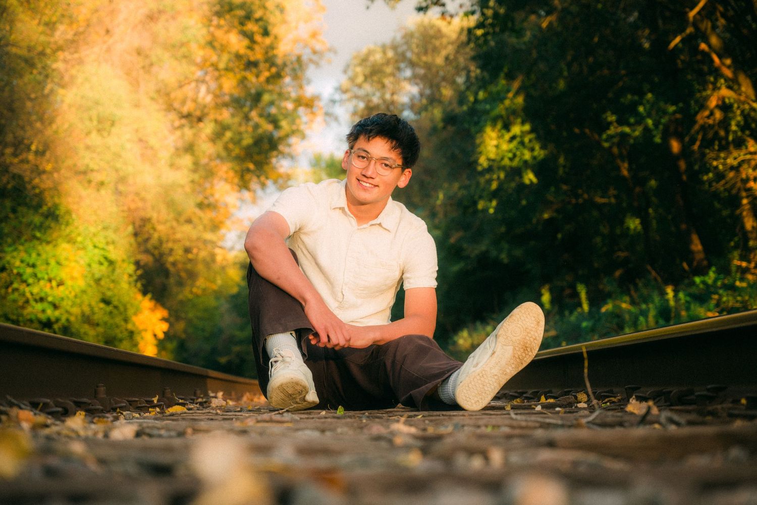 Person sitting on railroad tracks surrounded by autumn foliage in golden sunlight.