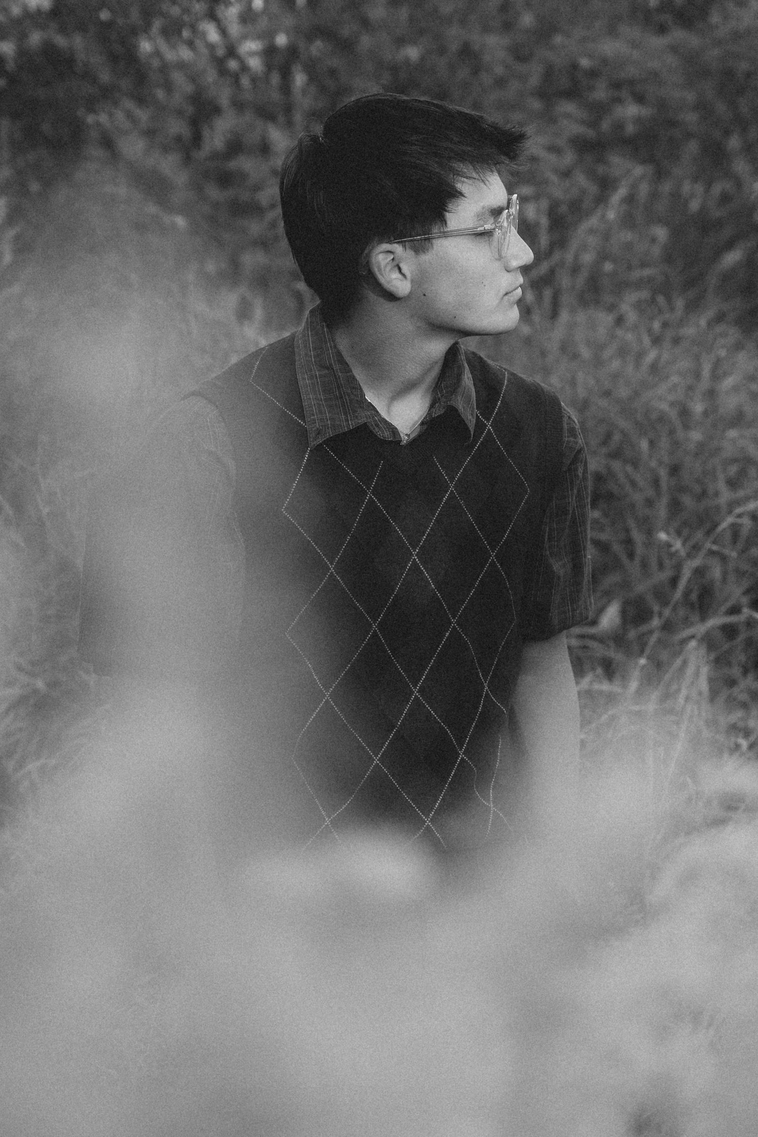Black and white portrait through misty foreground wearing argyle sweater.
