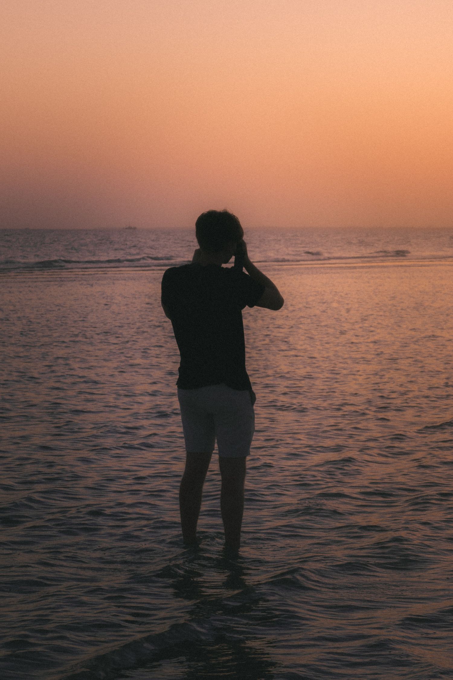 Silhouette of photographer capturing sunset while standing in ocean water.