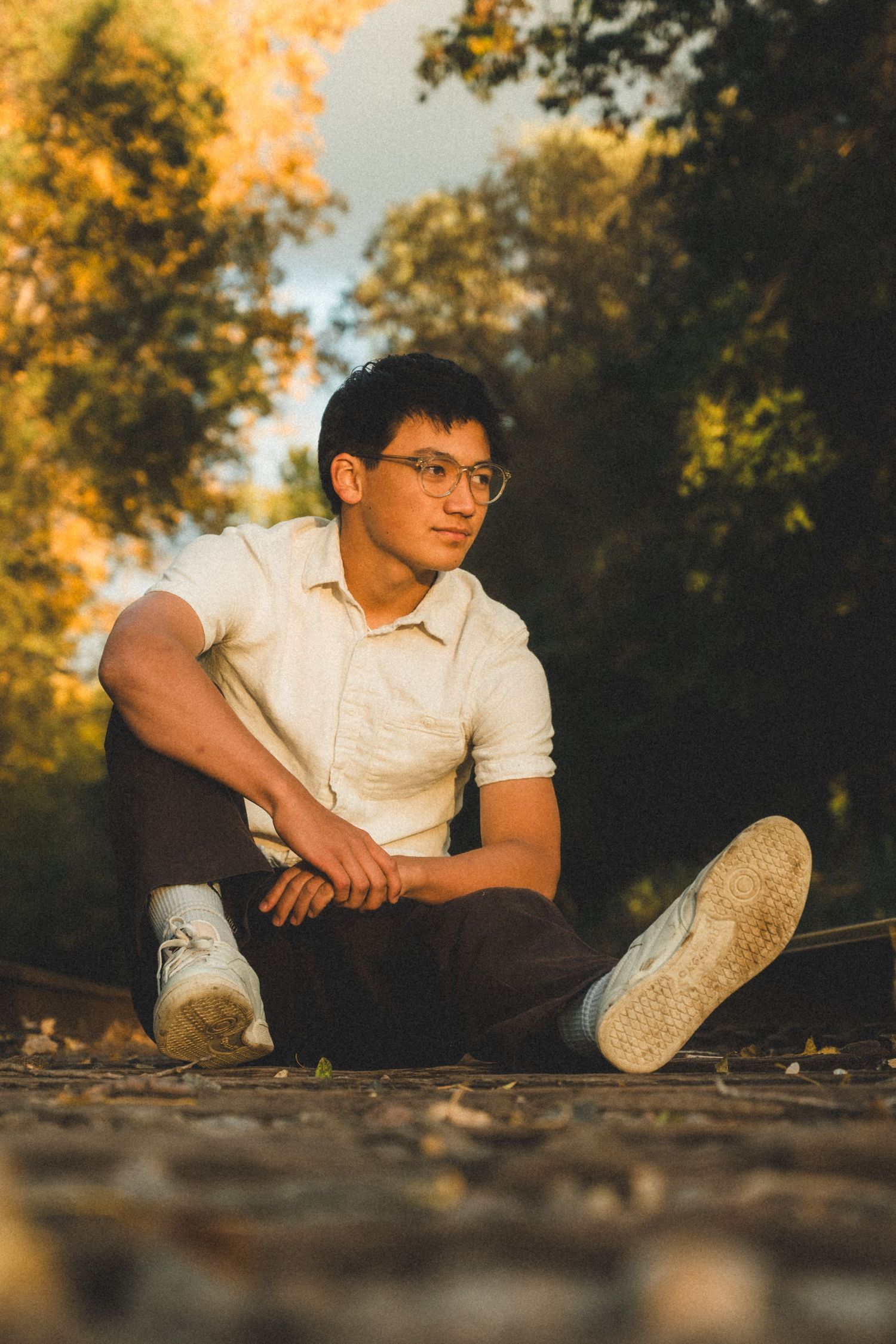 Casual portrait sitting on ground wearing white polo shirt and sneakers.