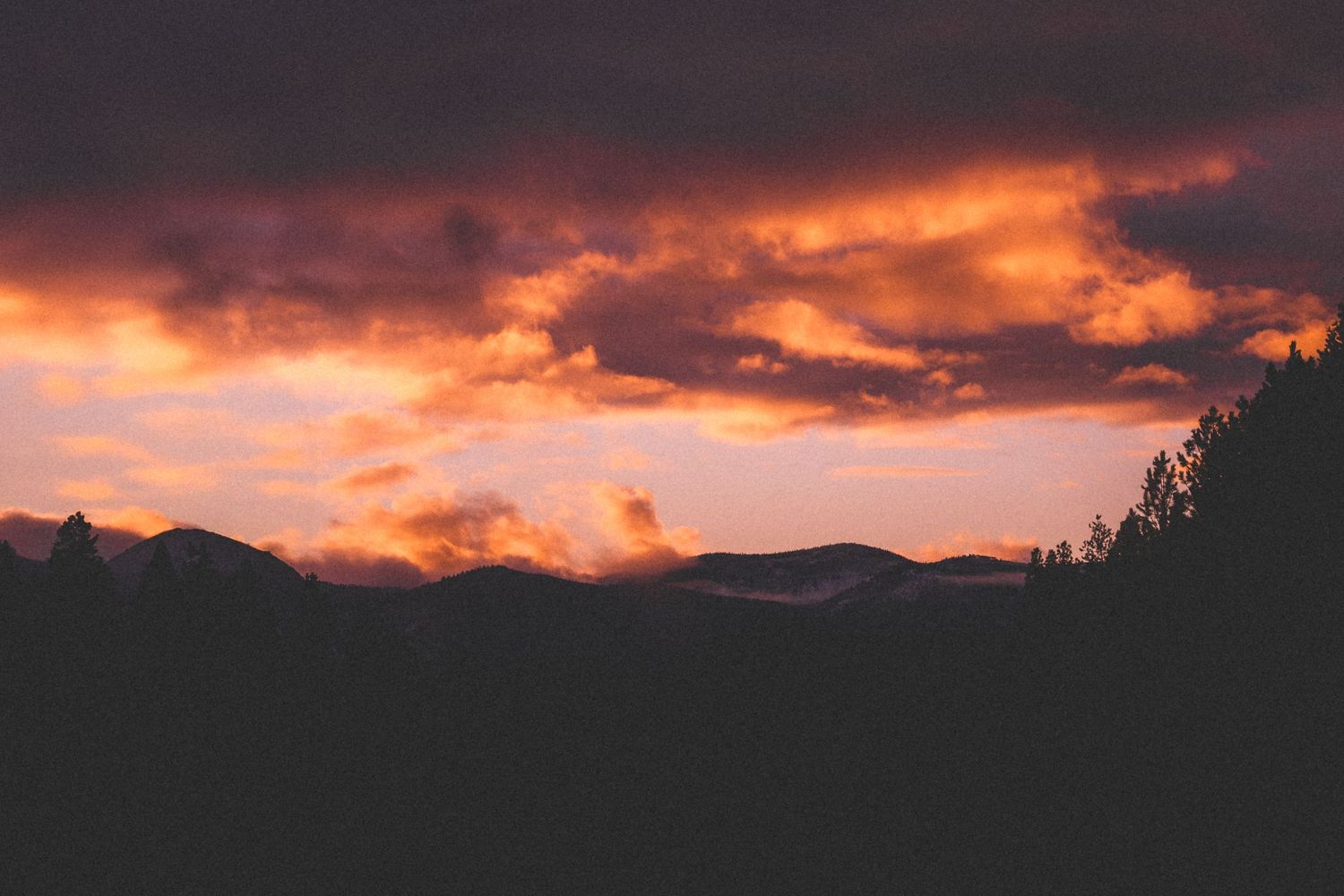 Dramatic orange sunset sky with dark clouds silhouetted against mountain peaks.