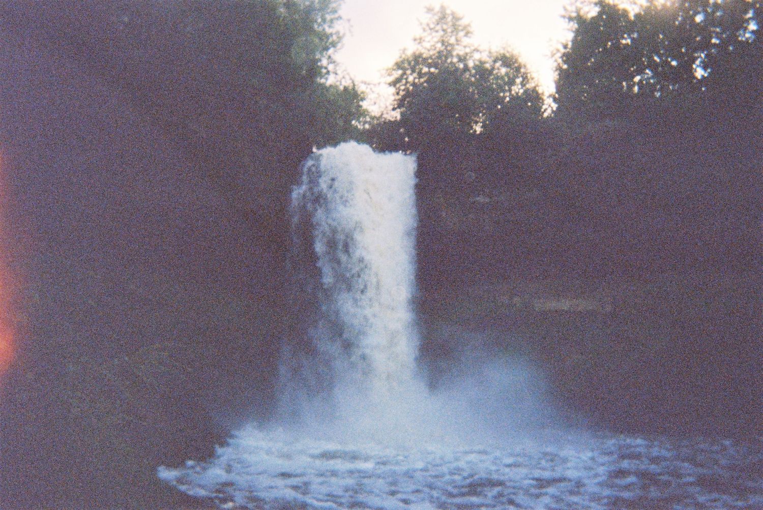 A serene waterfall cascades down rocks in a wooded setting at dusk.