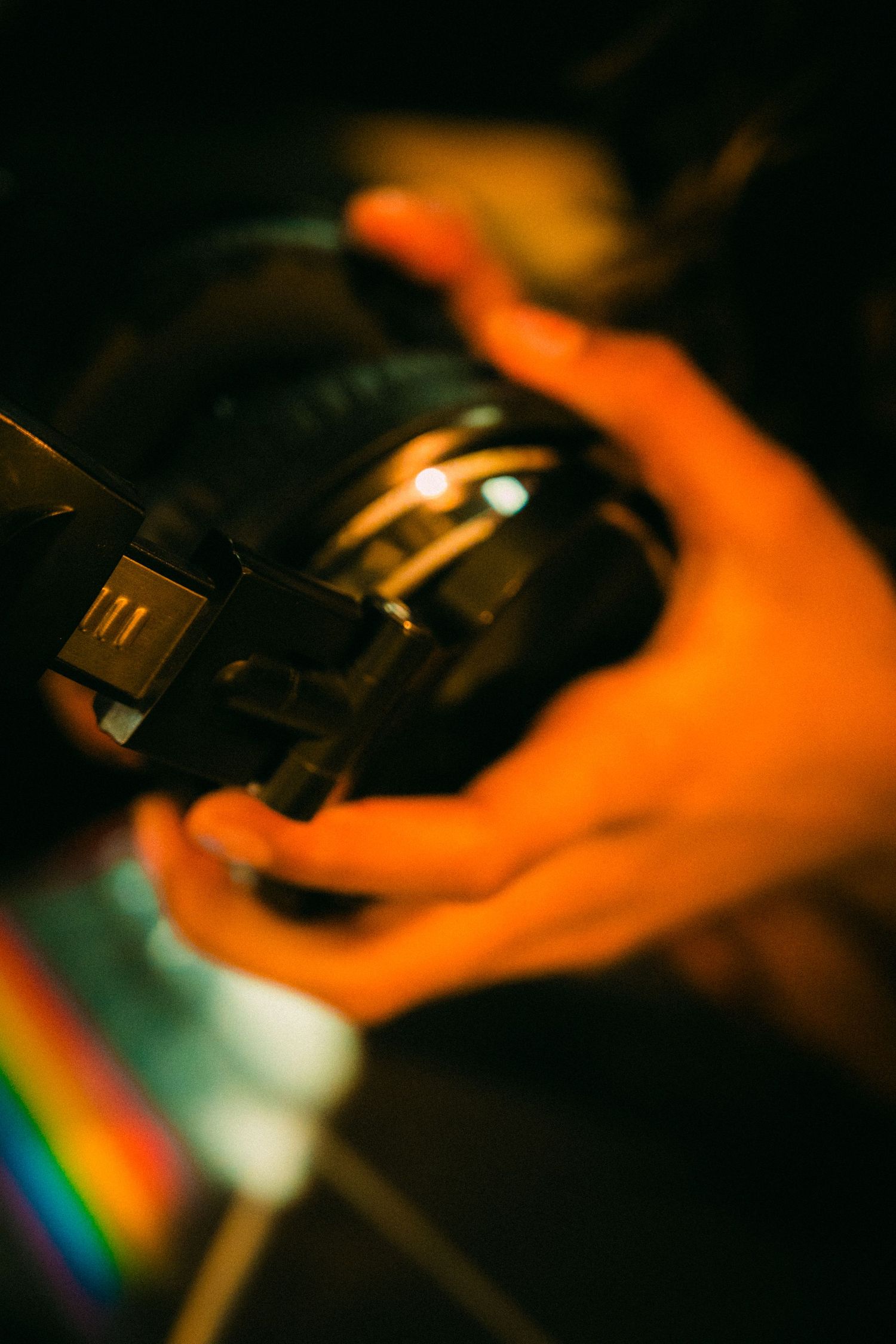 Close-up of hands adjusting a turntable needle with orange ambient lighting.