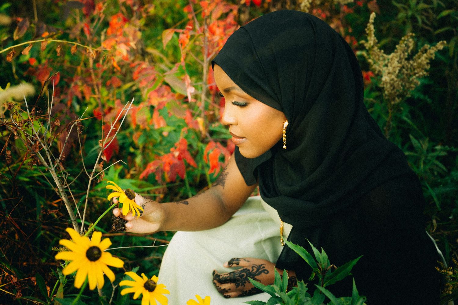 Person in black hijab observes yellow flowers in a vibrant garden setting.