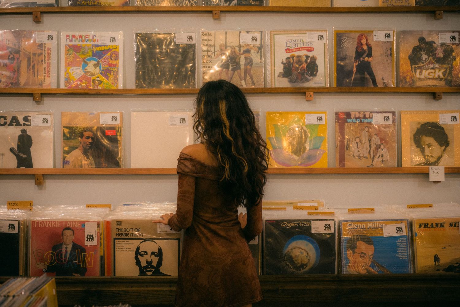 A vintage-style photo of someone browsing vinyl records displayed on wooden wall shelves.