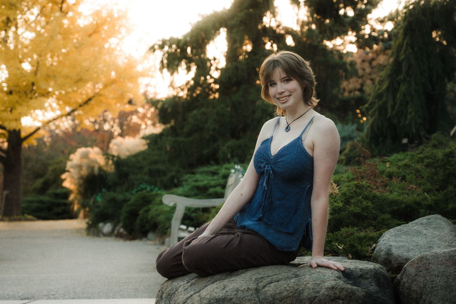 Person sitting on rock in garden during golden hour wearing navy tank top.