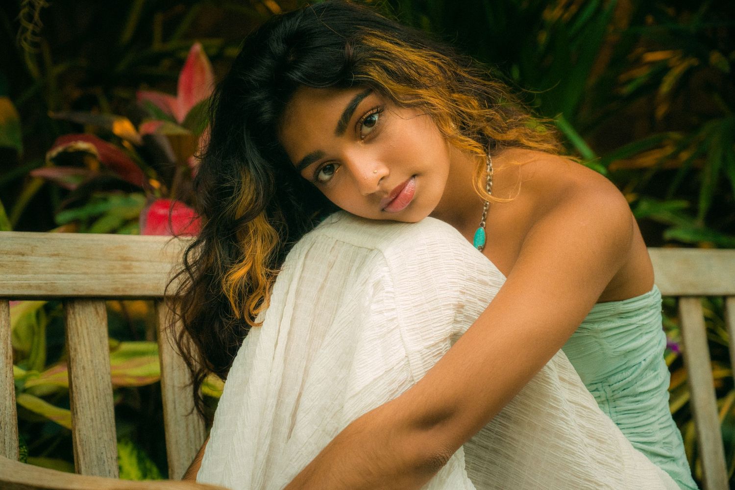 A candid portrait on a wooden bench surrounded by tropical plants.