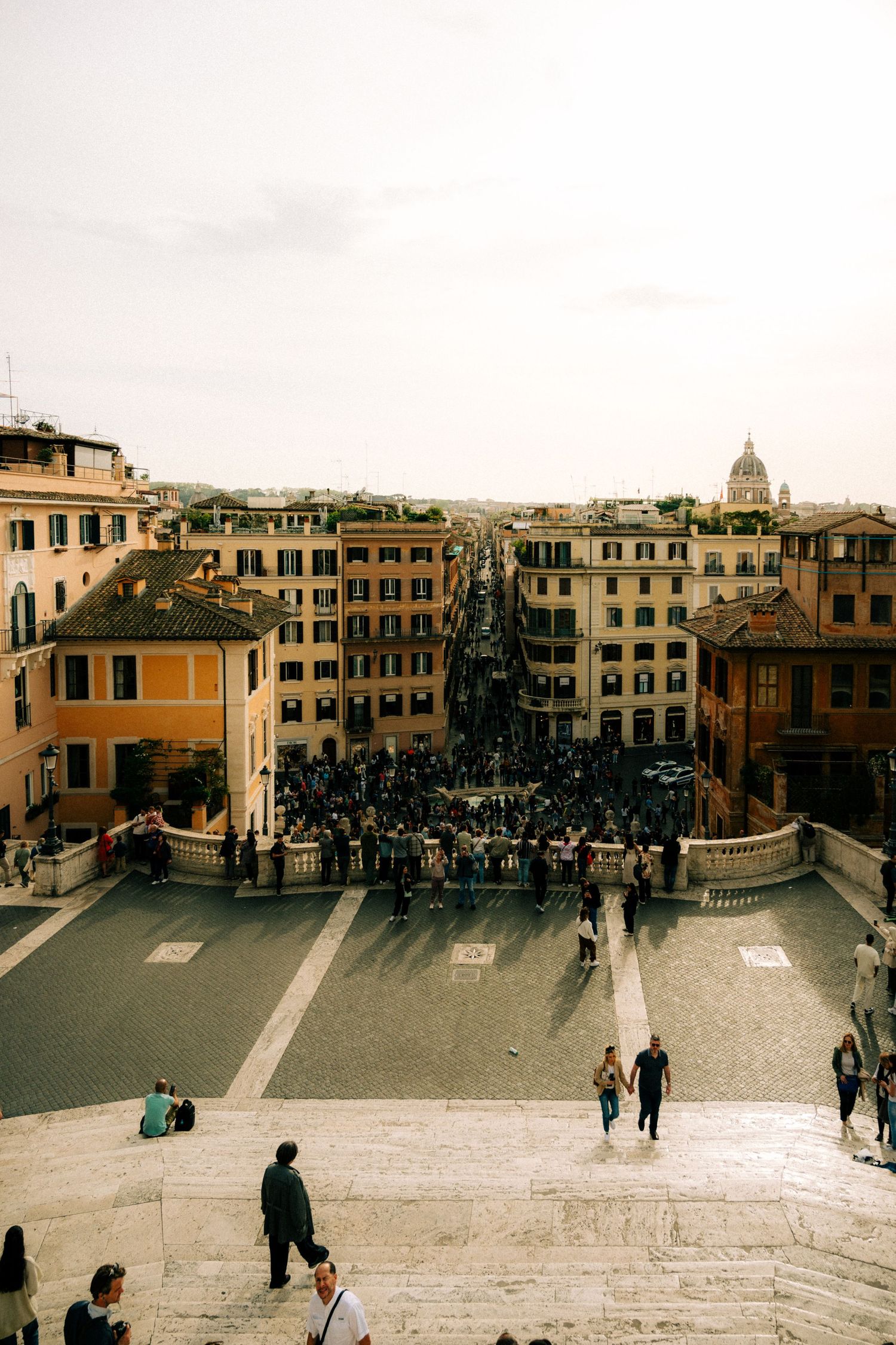 View down the Spanish Steps in Rome with historic buildings and crowds of tourists below.