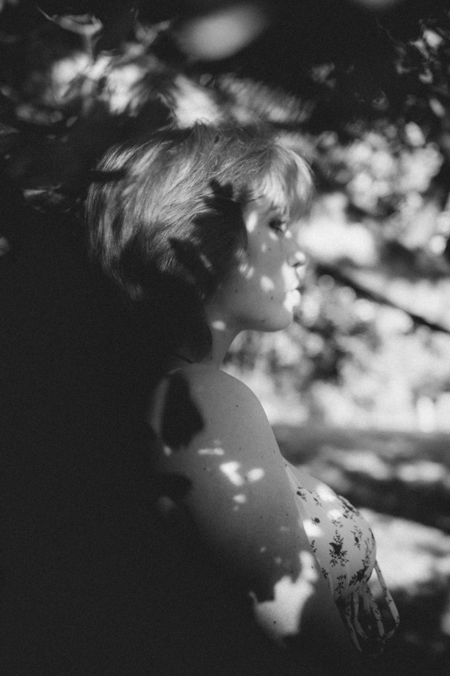 A dreamy black and white portrait with bokeh lighting effects through tree branches.