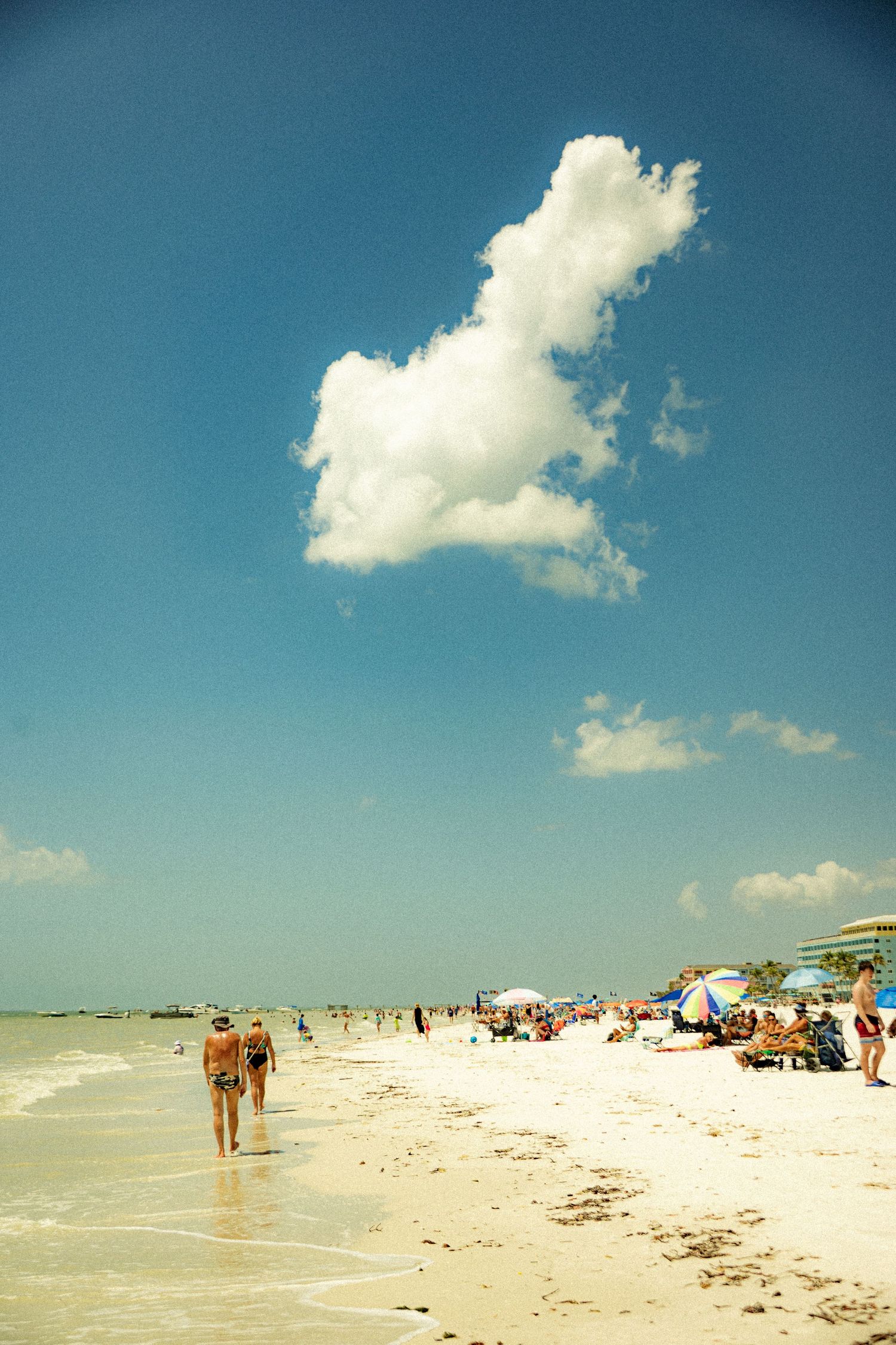 A sunny beach scene with white sand and people dotting the shoreline under a bright blue sky.