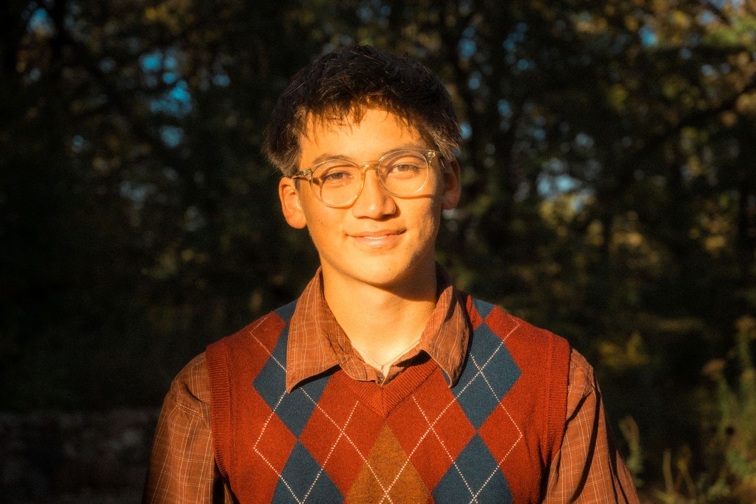 Person wearing argyle sweater vest standing outside in warm autumn lighting.