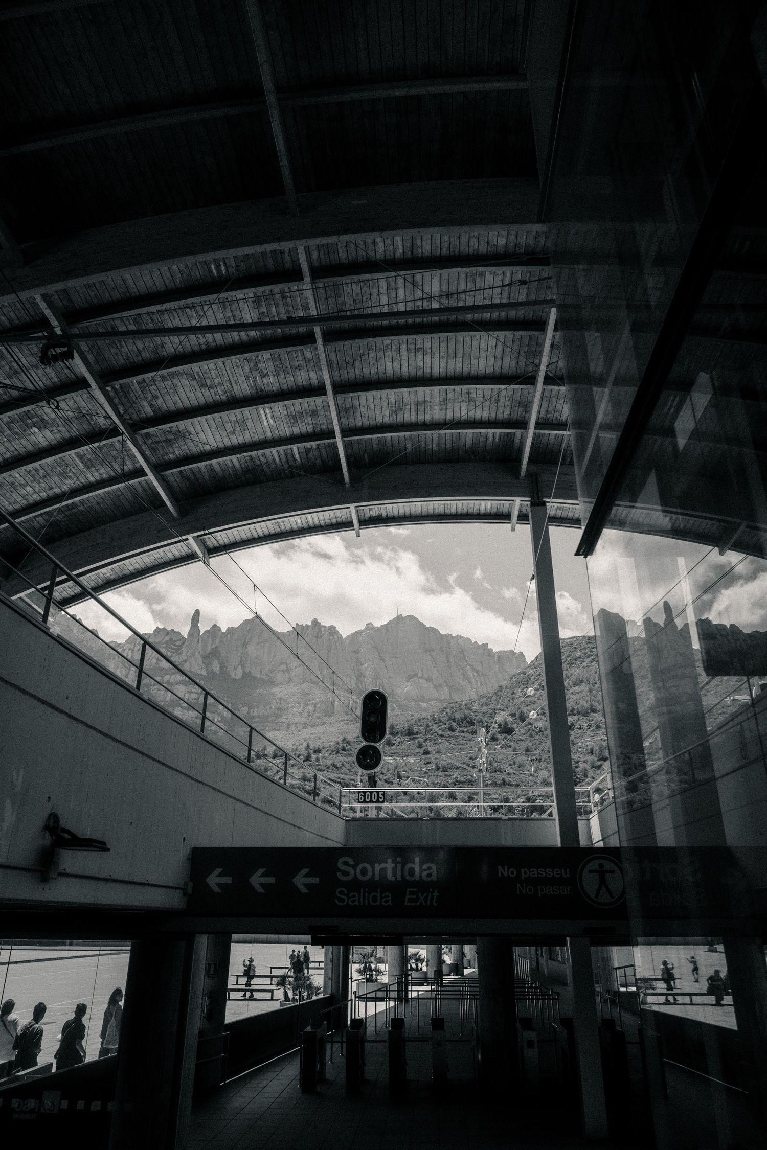Modern transit station interior with dramatic silhouetted figures against large windows and mountain backdrop.