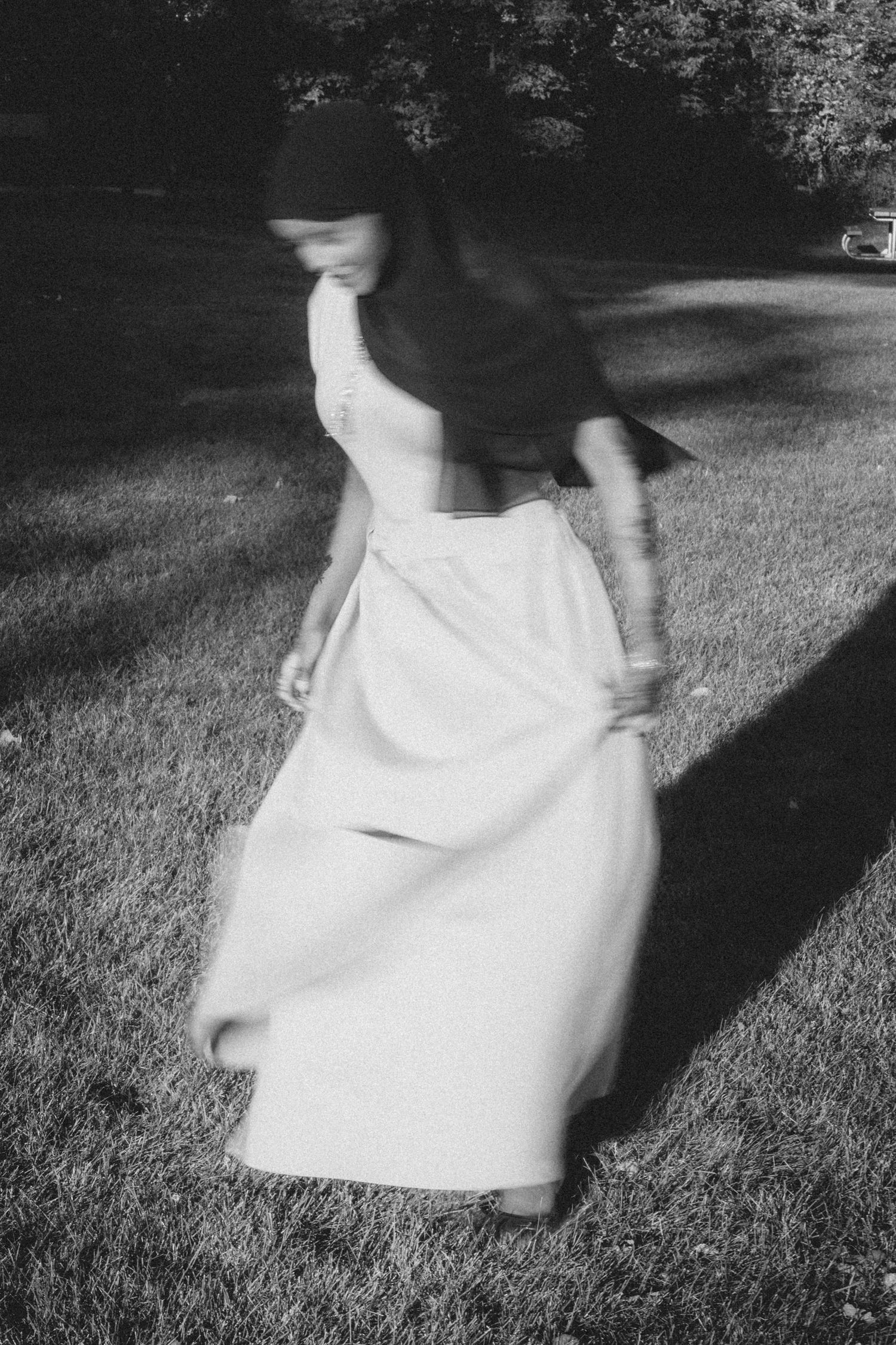 Motion-blurred black and white photo of person in flowing white dress spinning outdoors.