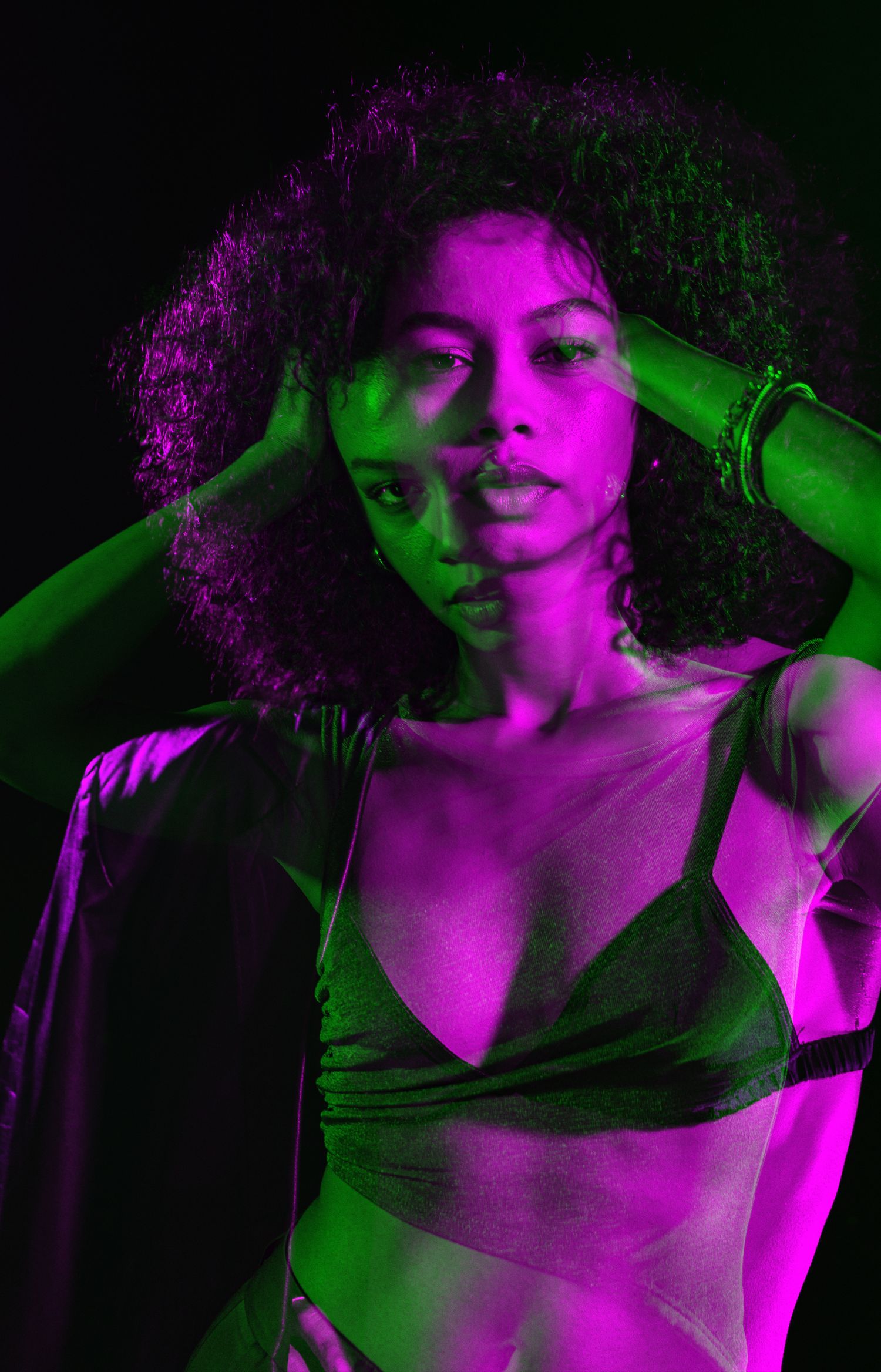 Portrait bathed in vibrant purple and green theatrical lighting.