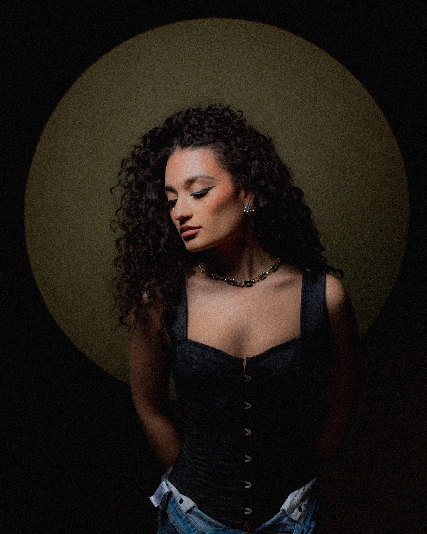 Dramatic low-key portrait in black corset and curly hair against dark background.