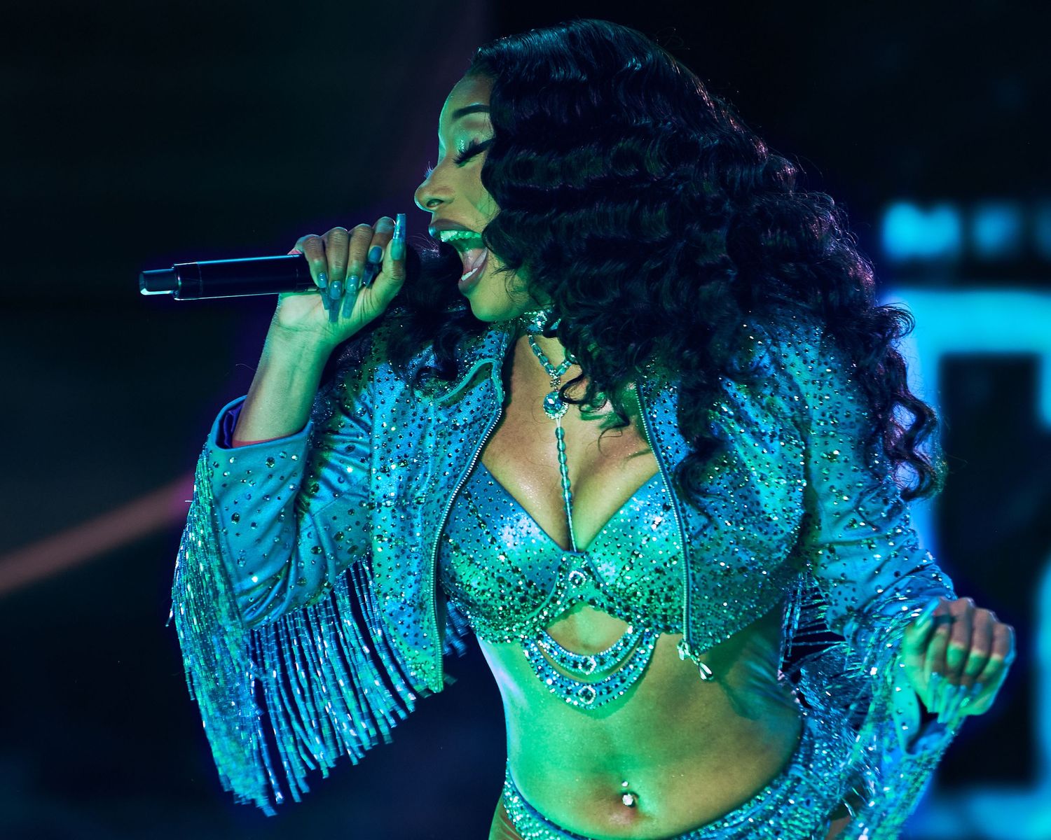Performer in turquoise sequined outfit dances under blue stage lighting. megan thee stallion