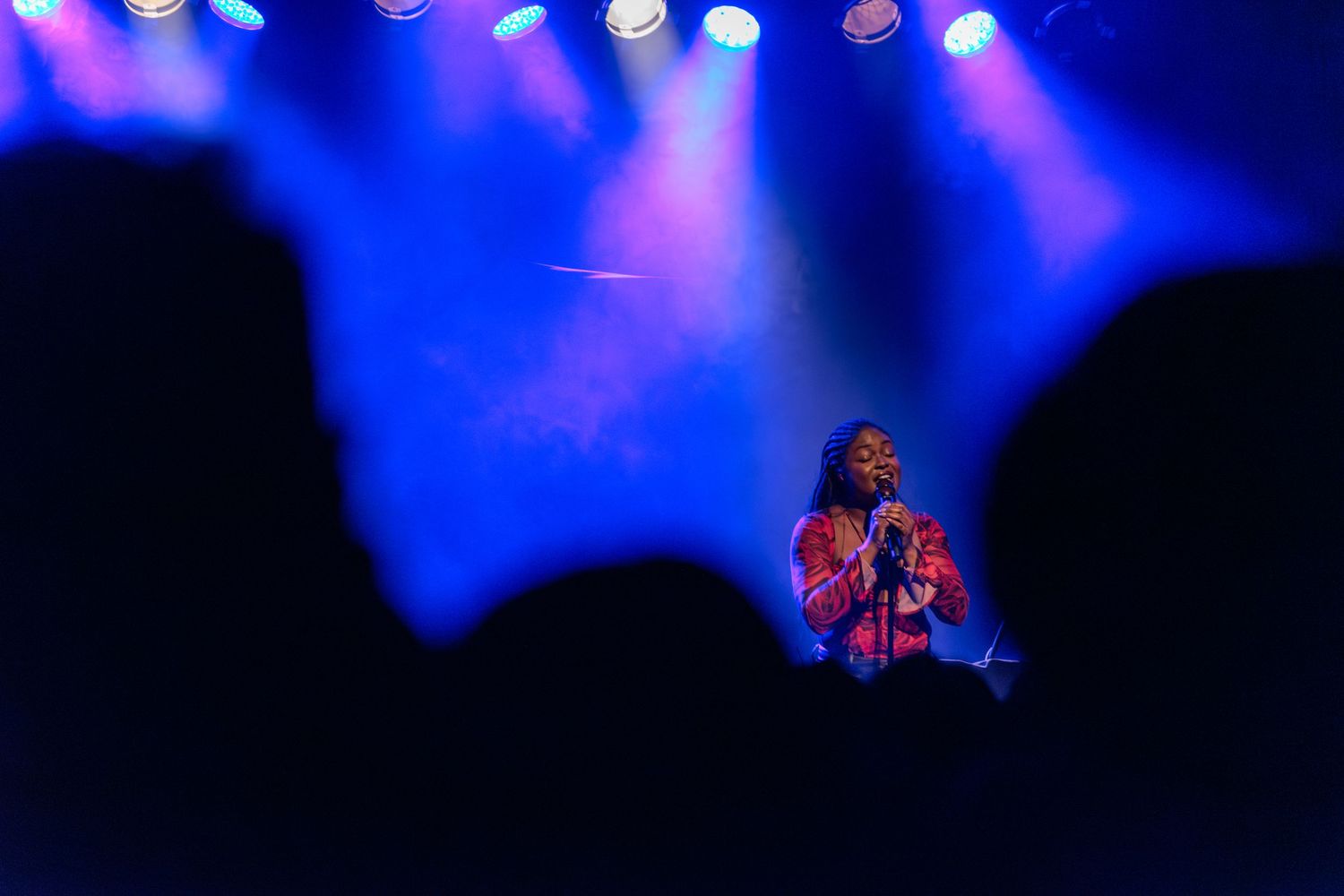 Concert venue with blue stage lighting and silhouetted crowd in the background. Aquila