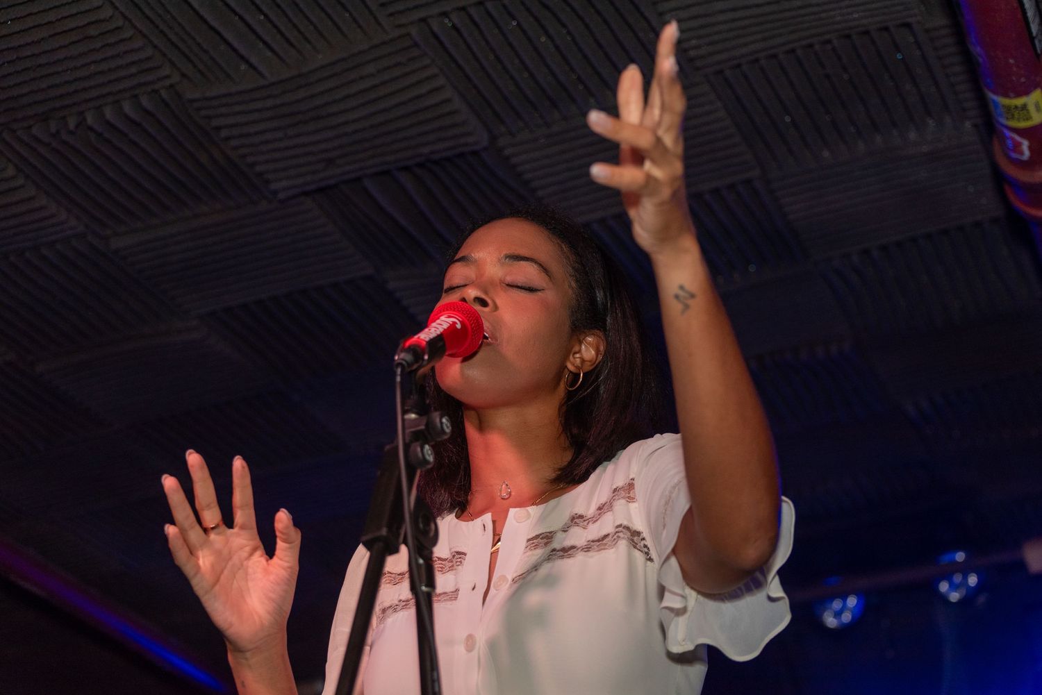 Singer gestures expressively while performing on stage with blue lighting effects.