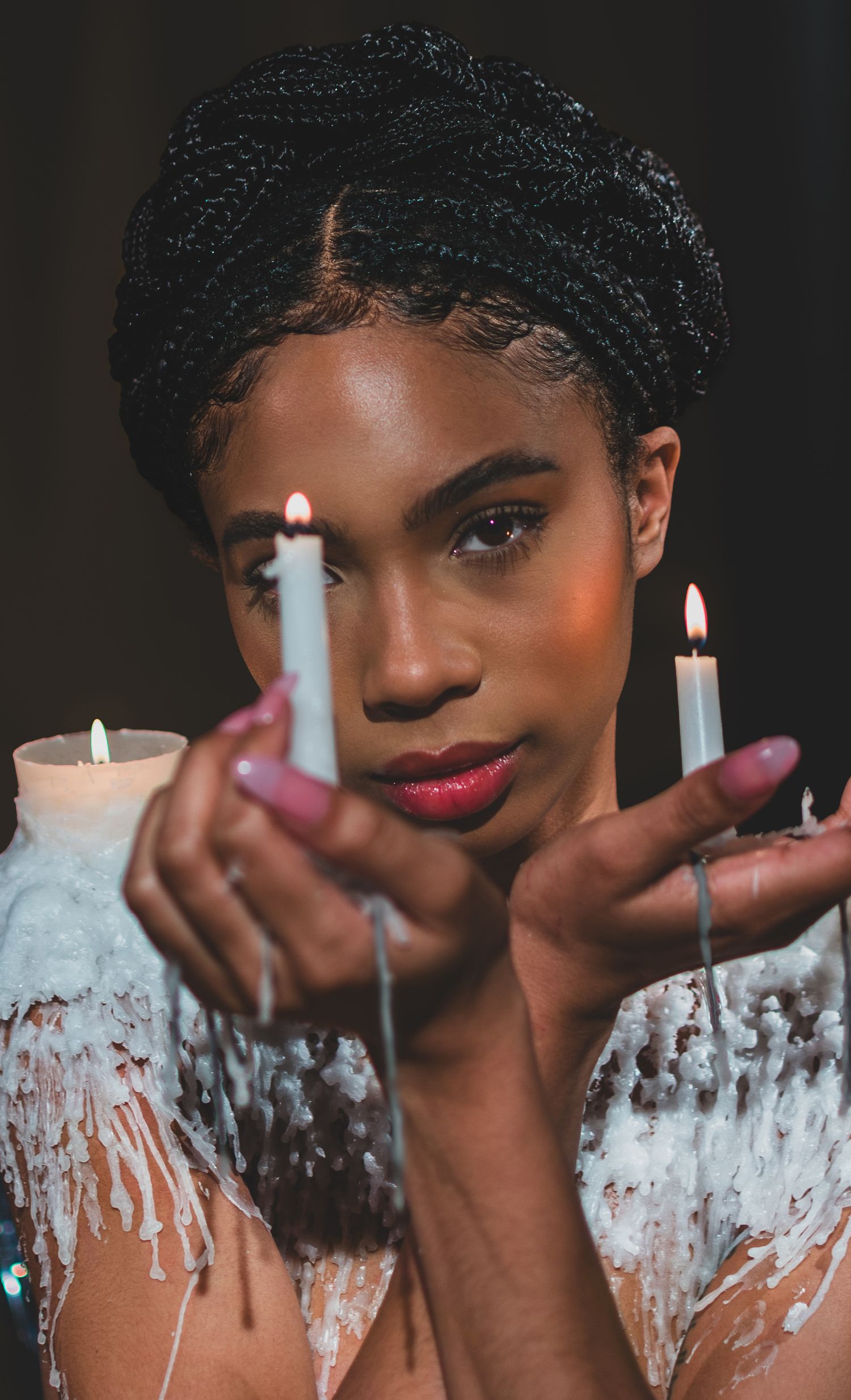 Artistic portrait with lit candles creating a dreamy atmosphere against dark background. with candle wax clothing
