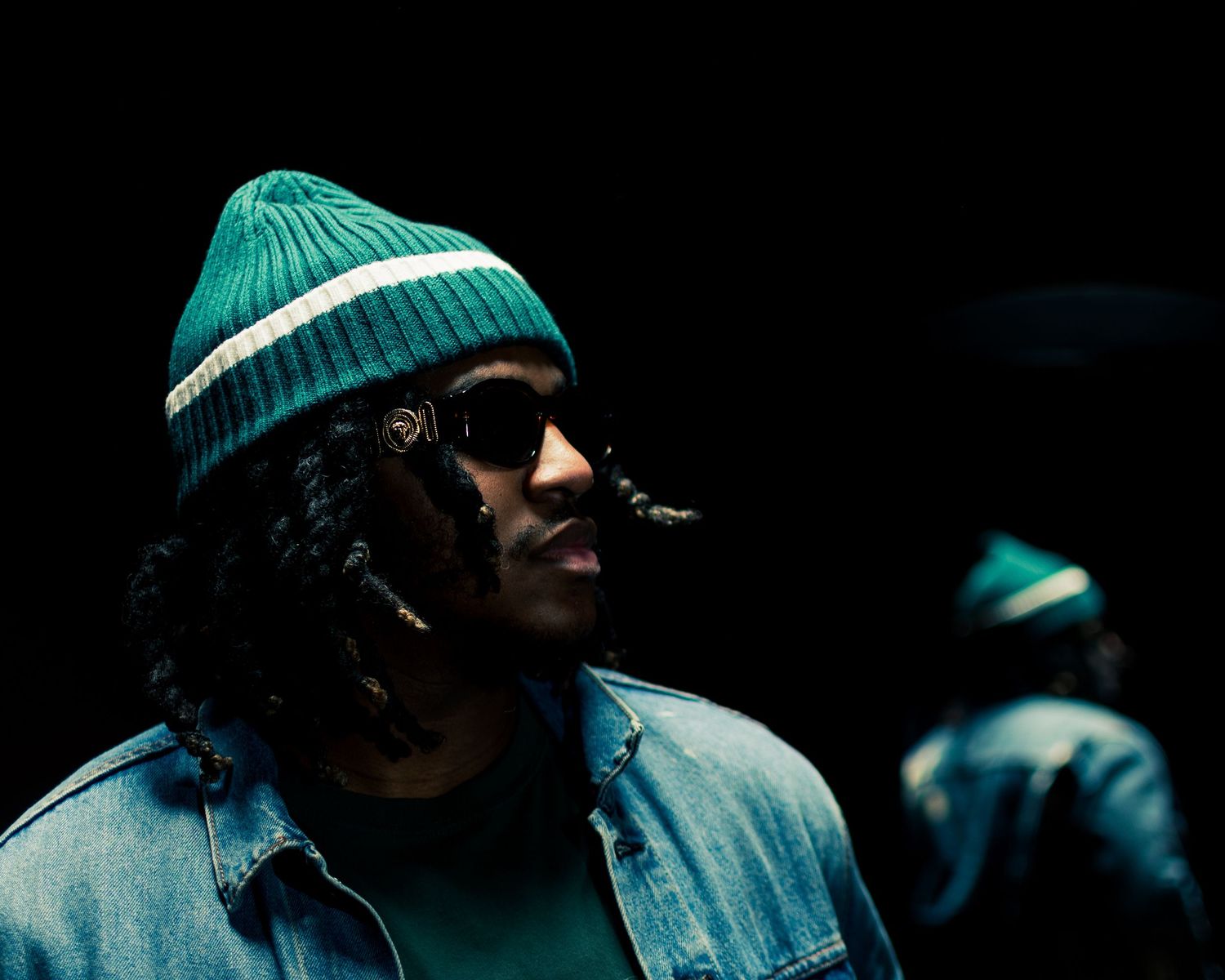 Artistic profile shot of performer wearing turquoise beanie in moody lighting.