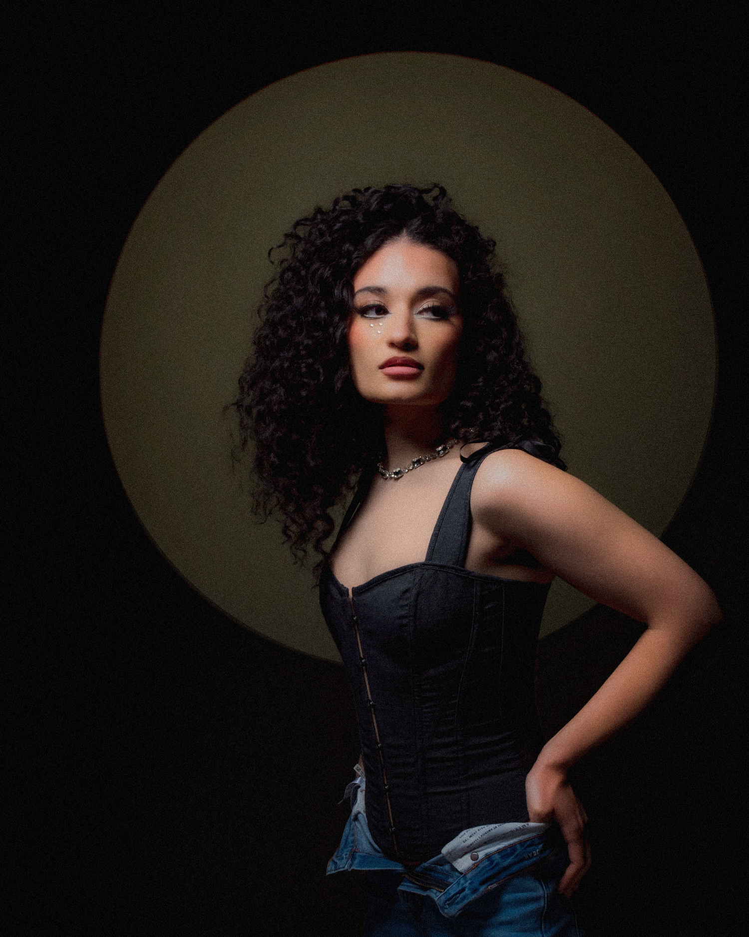 Artistic portrait with curly hair and black corset in dramatic shadows.