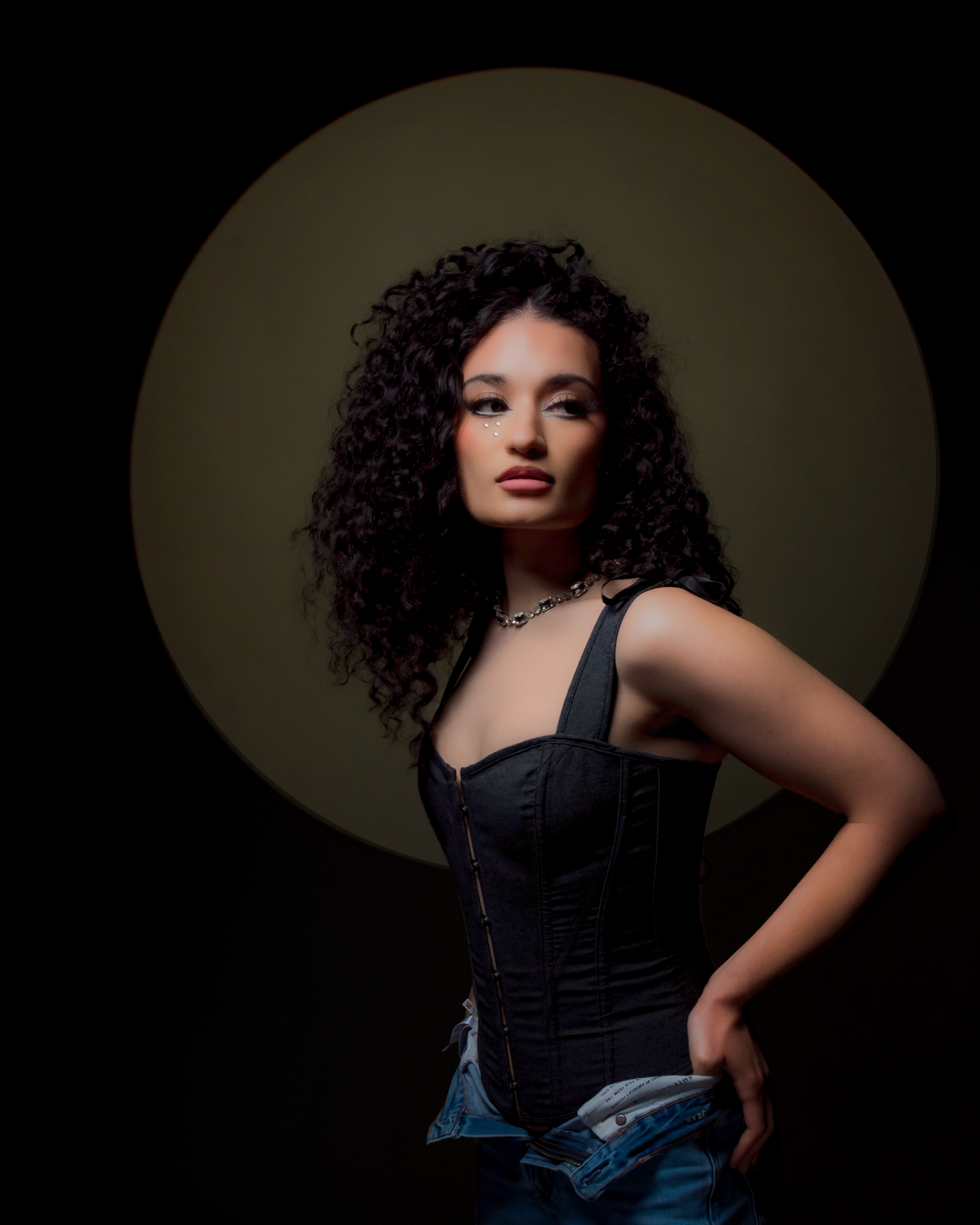 Artistic photoshoot featuring curly hair and black corset against moody lighting.