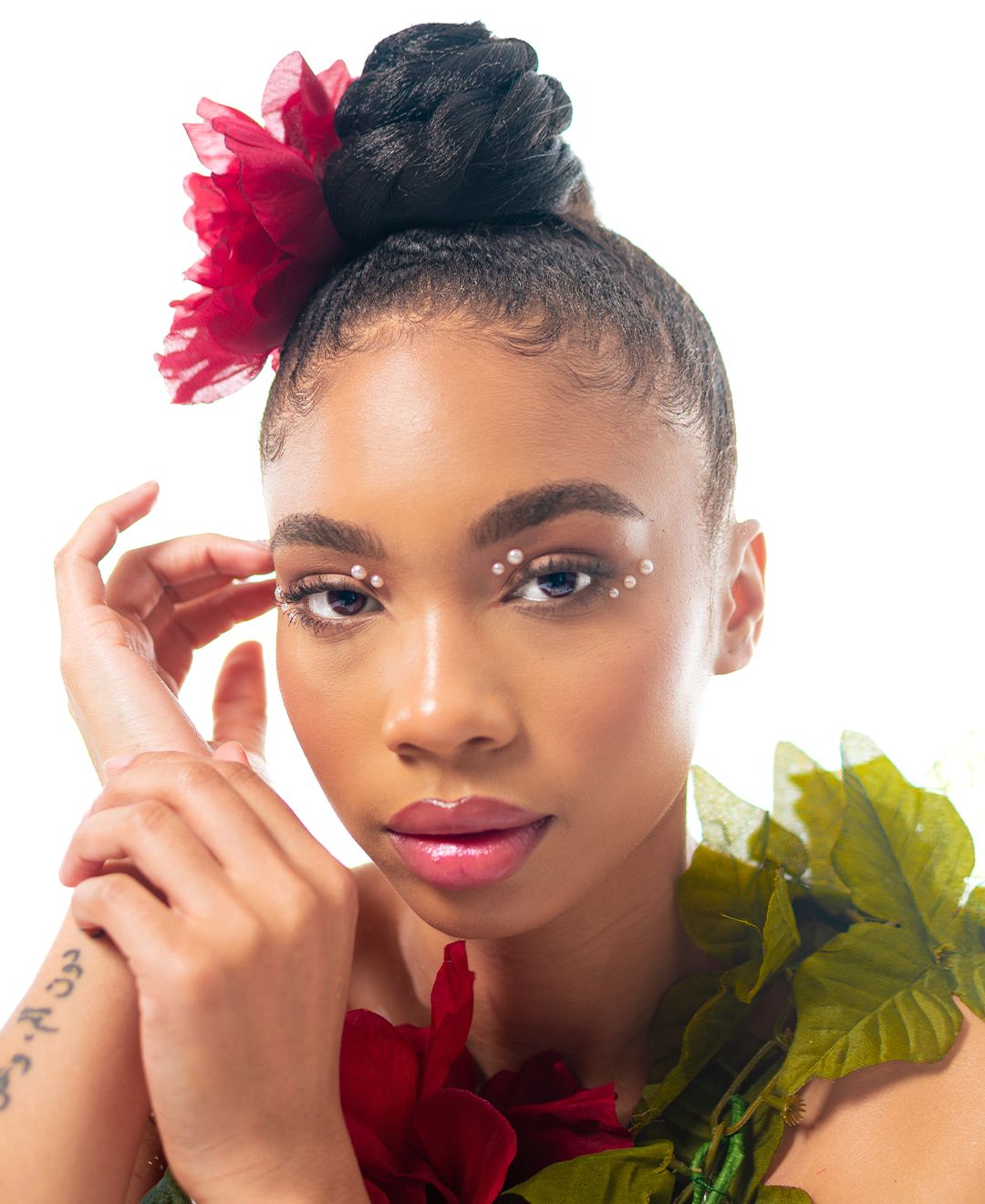 Artistic beauty portrait with pink floral accessories and green leaves creating a vibrant fashion editorial look.
