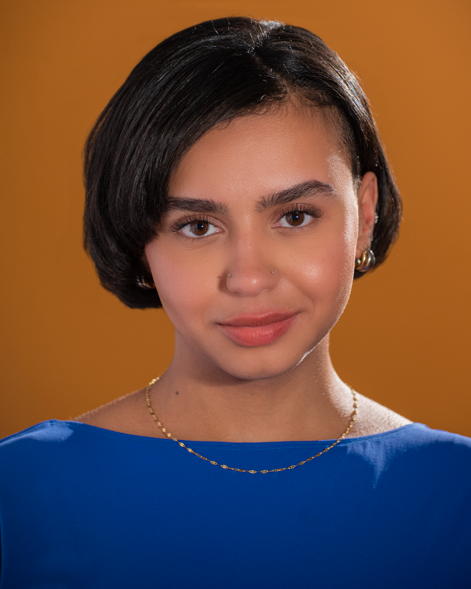 Elegant portrait in blue top against warm orange background with delicate necklace.