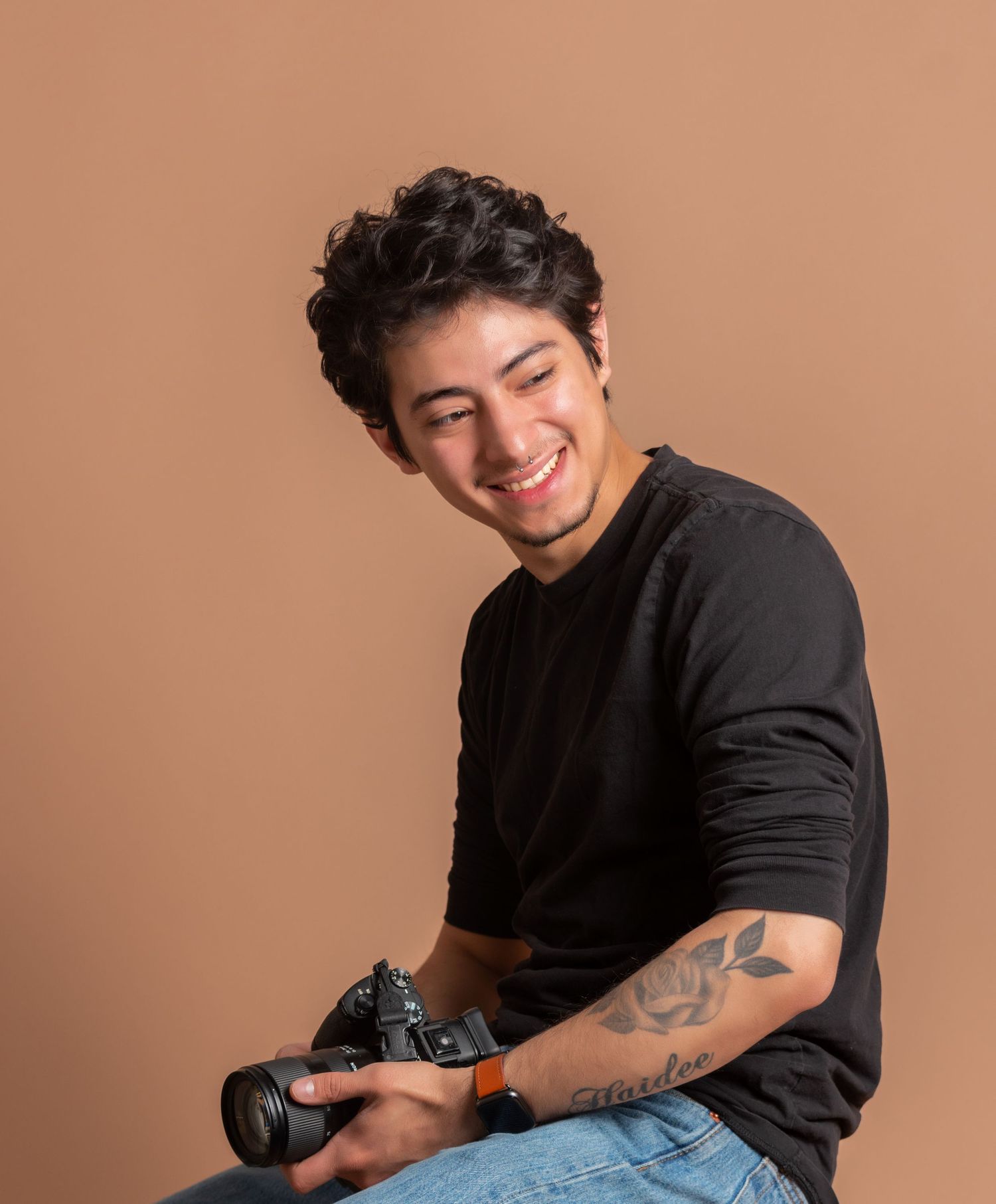 Casual studio portraits showing tattoos and black t-shirt against beige background.