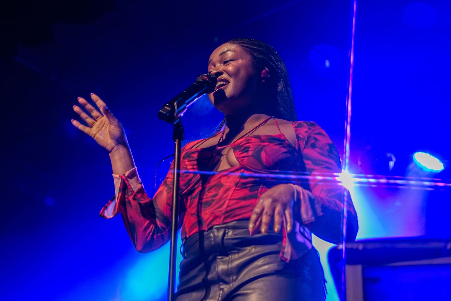 Concert performer in red outfit singing passionately on stage with dramatic blue lighting. Aquila
