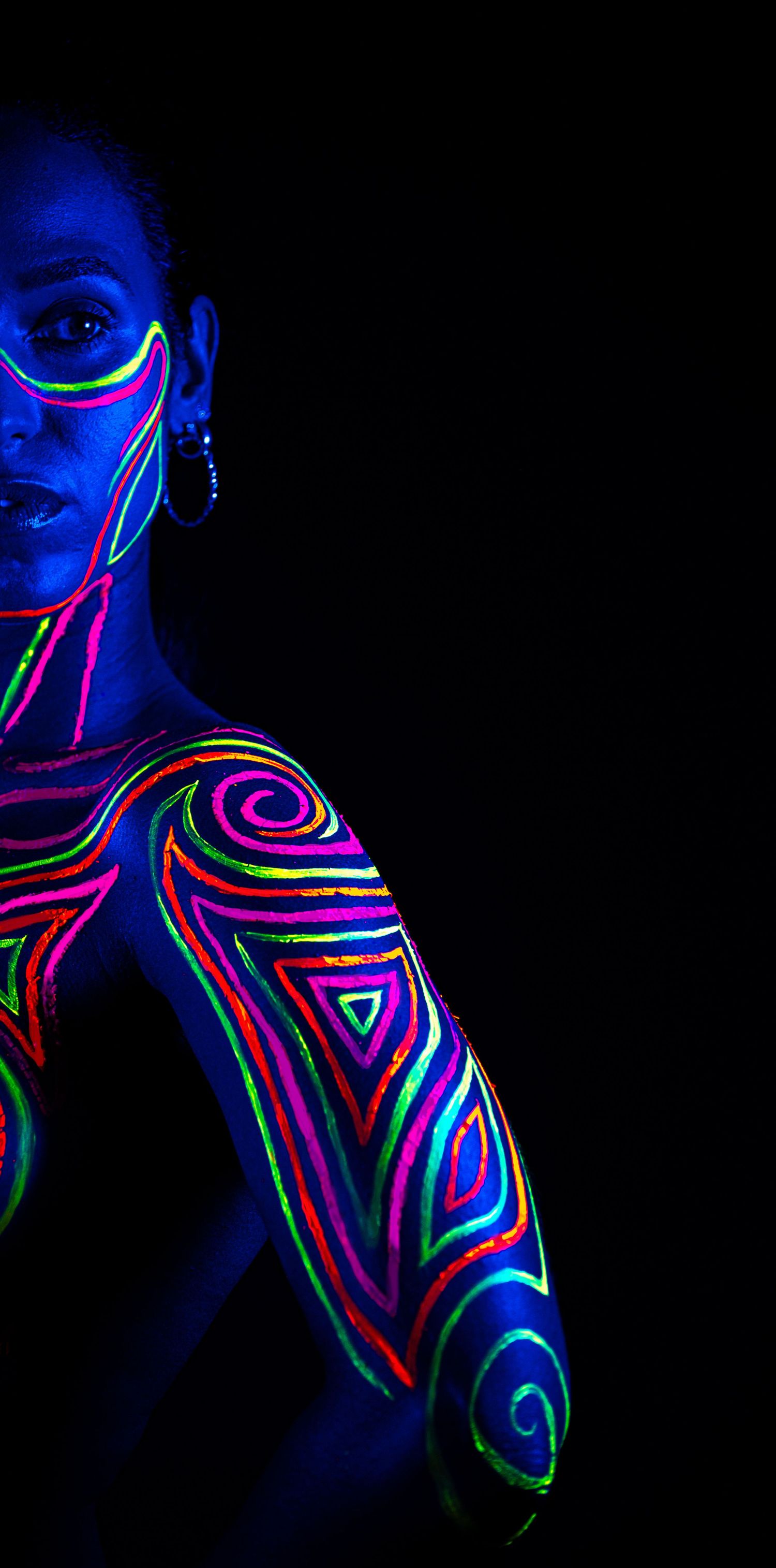 Artistic body painting with neon geometric patterns glowing under blacklight against dark background.