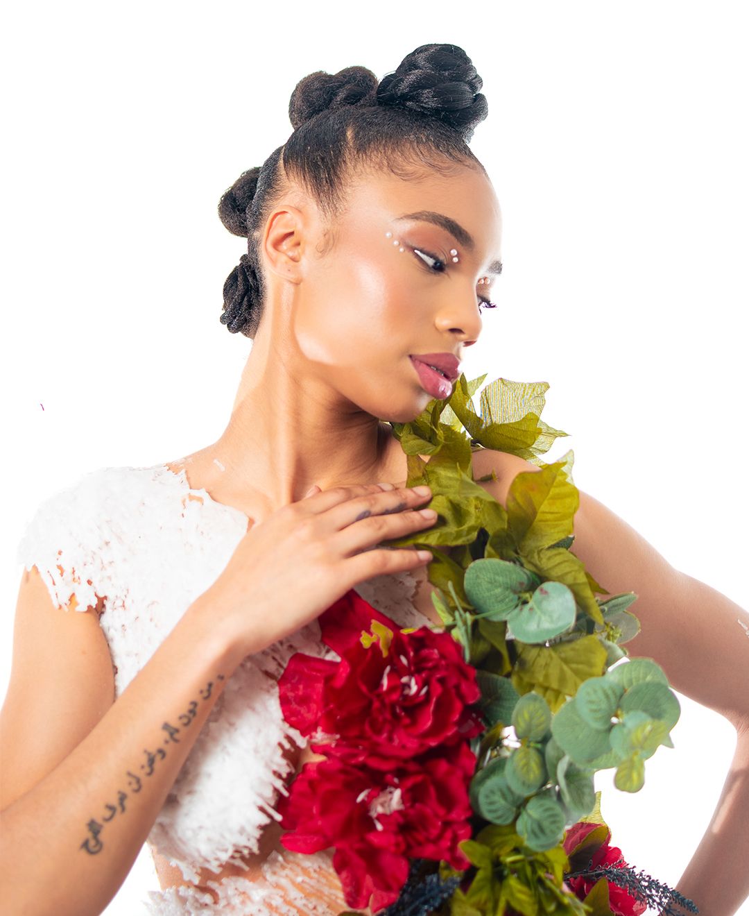 A person in a white lace dress poses with a vibrant red bouquet and eucalyptus against a light background.