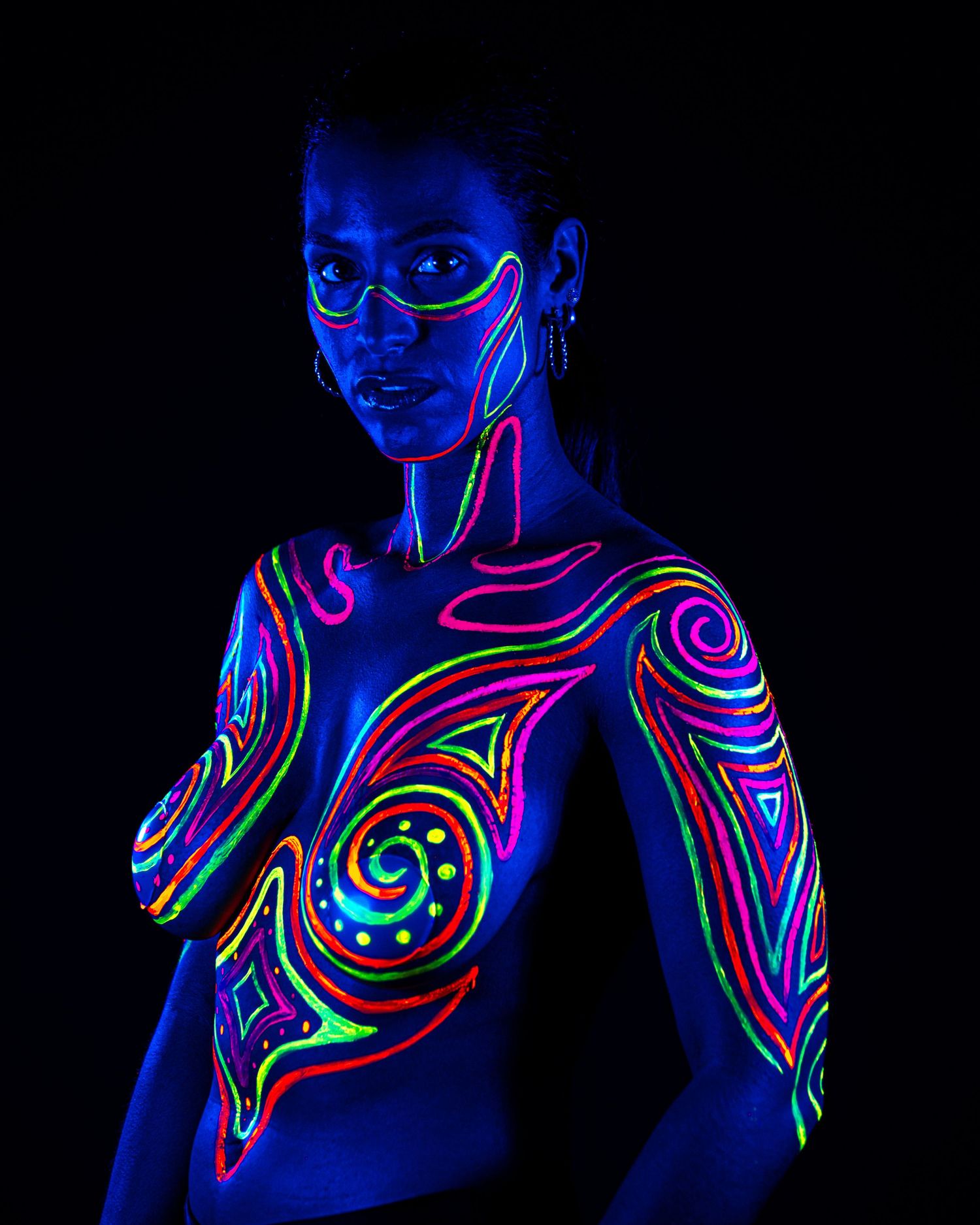 Fluorescent body paint design with spiral patterns and dots glowing vibrantly in ultraviolet lighting.